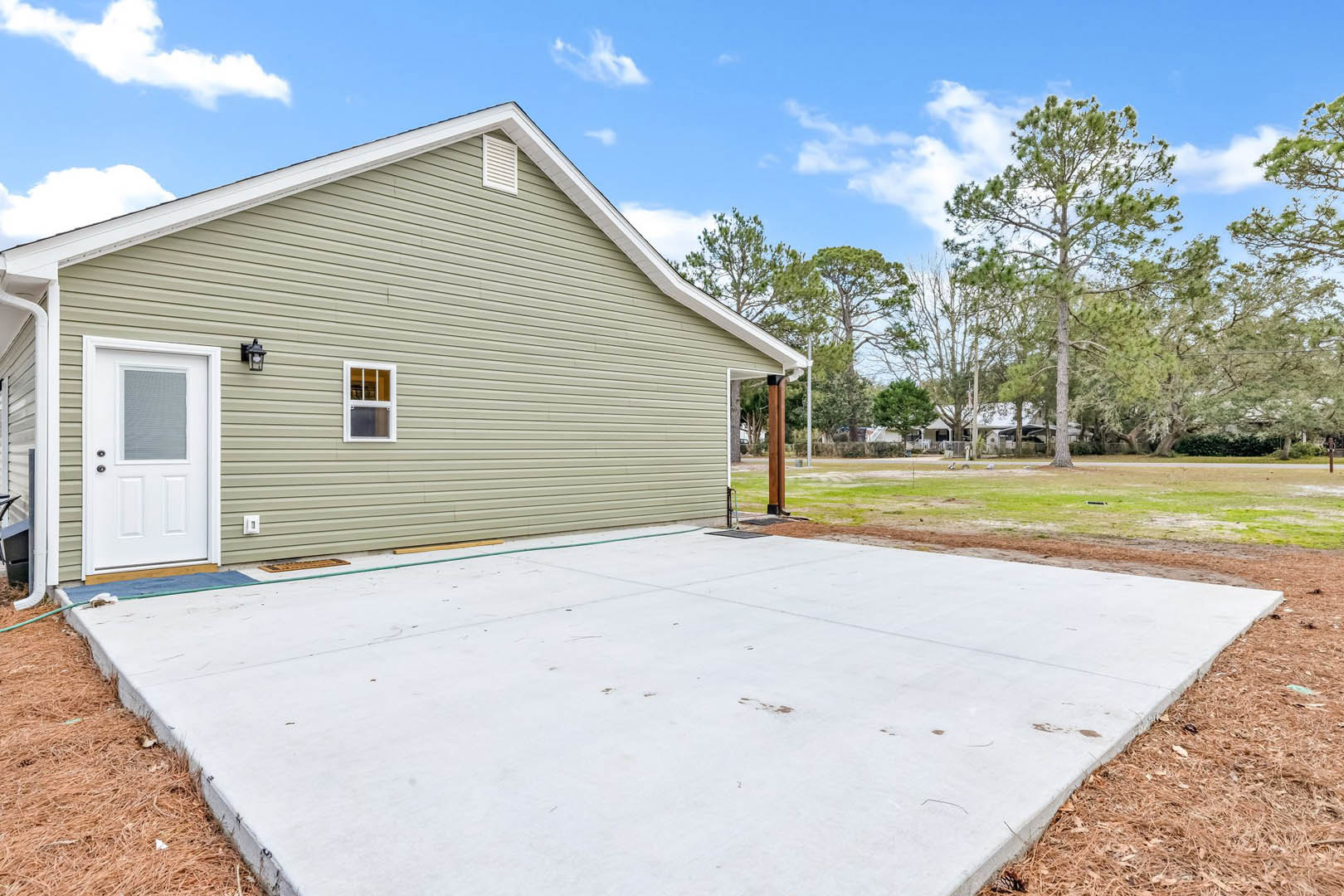 Two-story home with light siding, attached garage, concrete patio, white doors and windows, grassy lawn, and trees under a cloudy sky