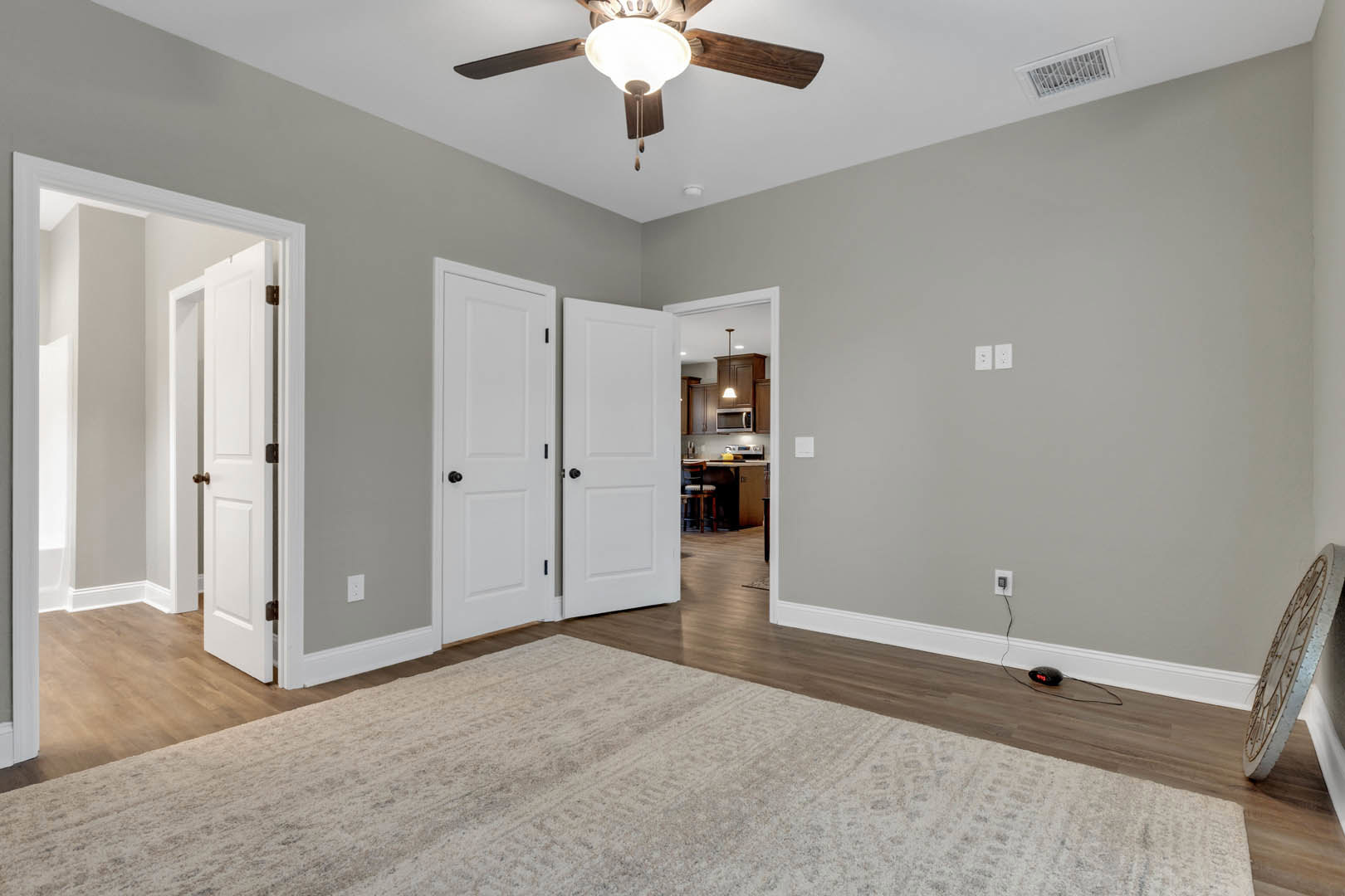 White paneled doors with black knobs, patterned rug on hardwood floor, wall clock, ceiling fan with light fixture, neutral walls