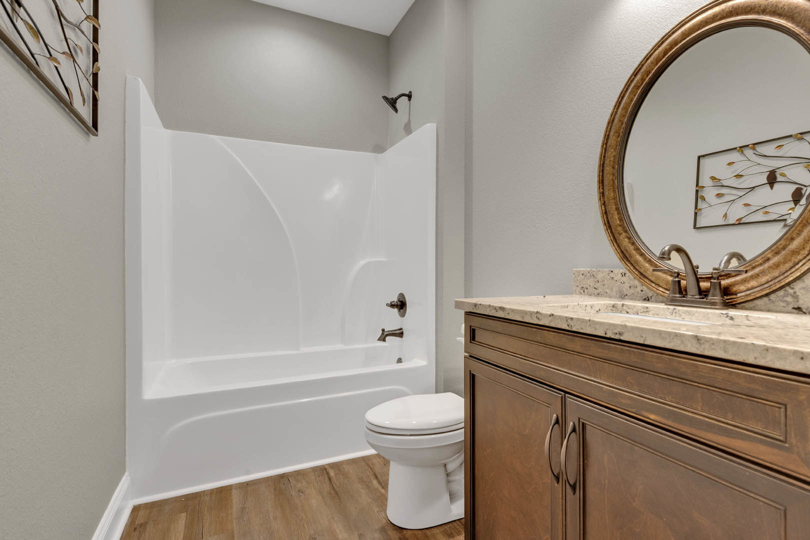 Modern bathroom with white porcelain sink and toilet, wall-mounted mirror above vanity, decorative metal art and framed picture, tiled walls, and white bathtub.