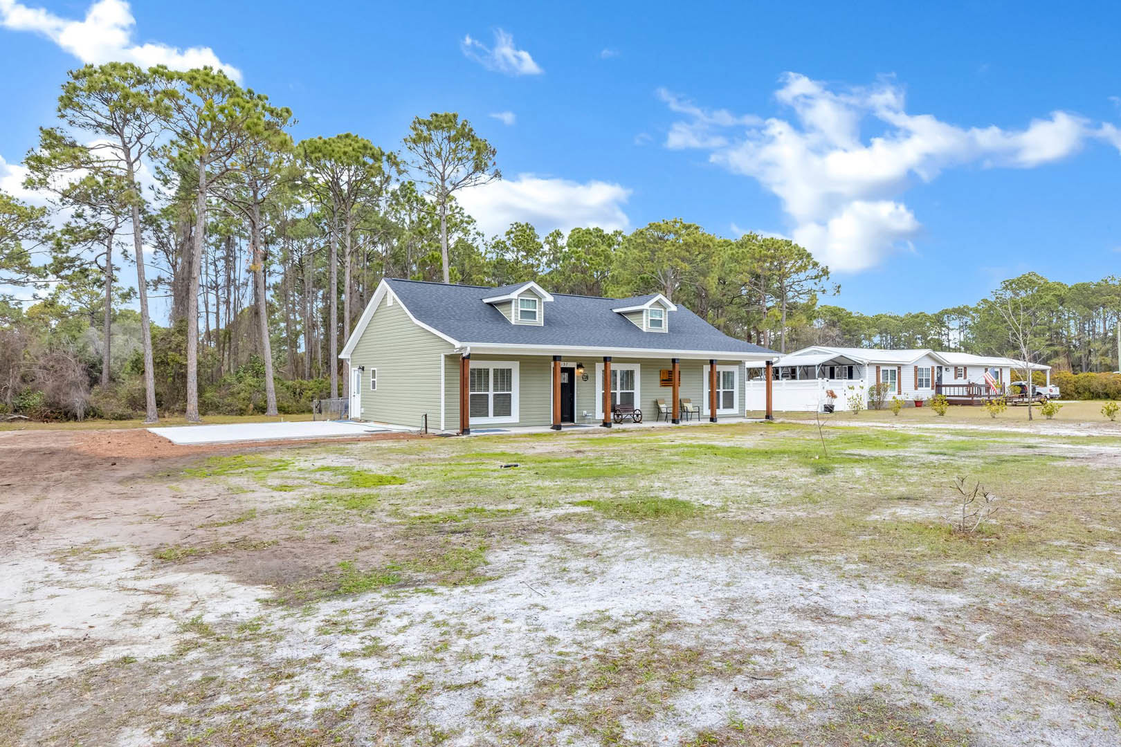 White house with brown shutters and front porch, surrounded by tall trees and grassy lawn with a bench; white windows with vents visible.