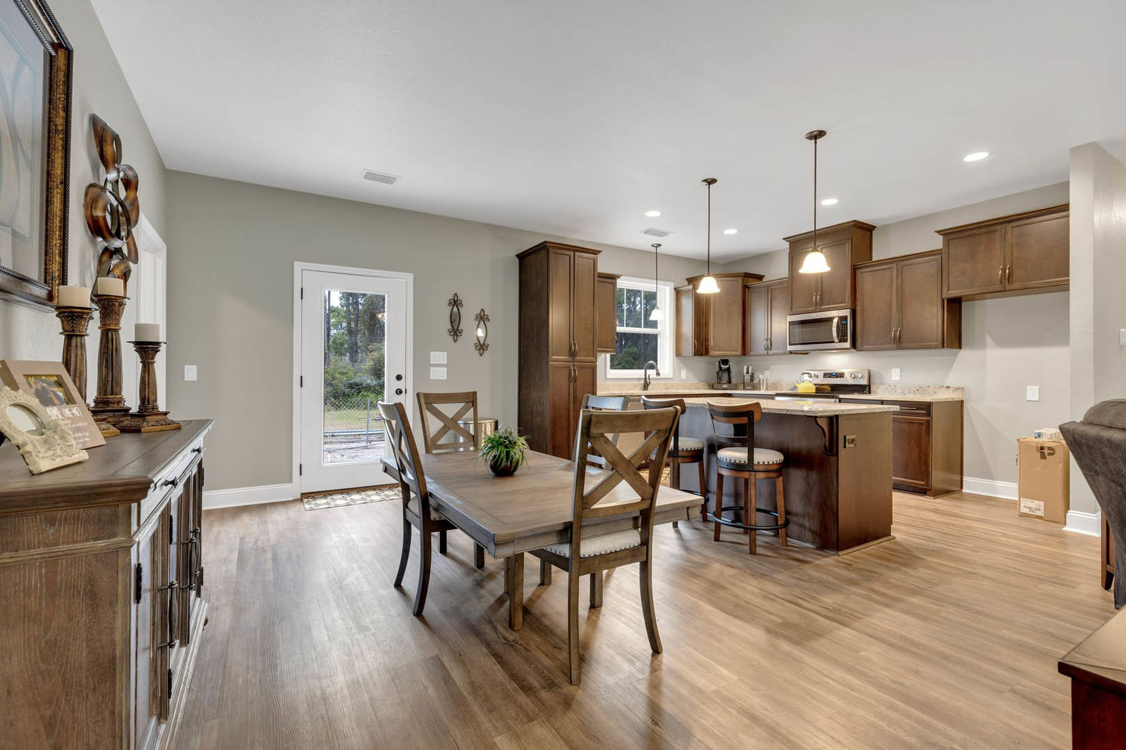 Open kitchen and dining area with wood table, upholstered chairs, potted plant centerpiece, white cabinetry, stainless microwave, light walls, and hardwood flooring