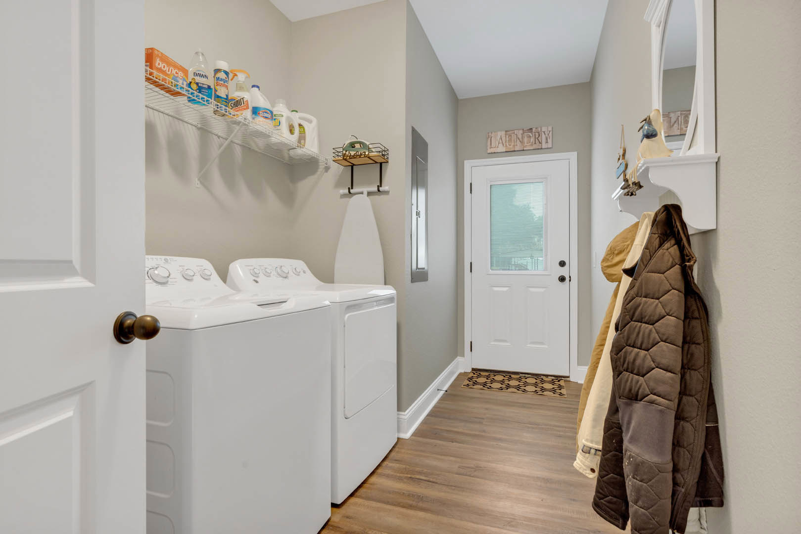 Laundry room with white washer and dryer, wood flooring, white door with window, brown jacket hanging on coat rack, cabinetry and drawers along wall
