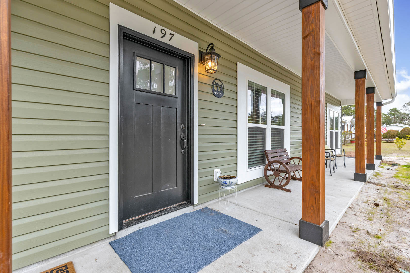 Front porch with white siding, black door, blue rug, decorative bowl on a stand, and wall-mounted light fixture
