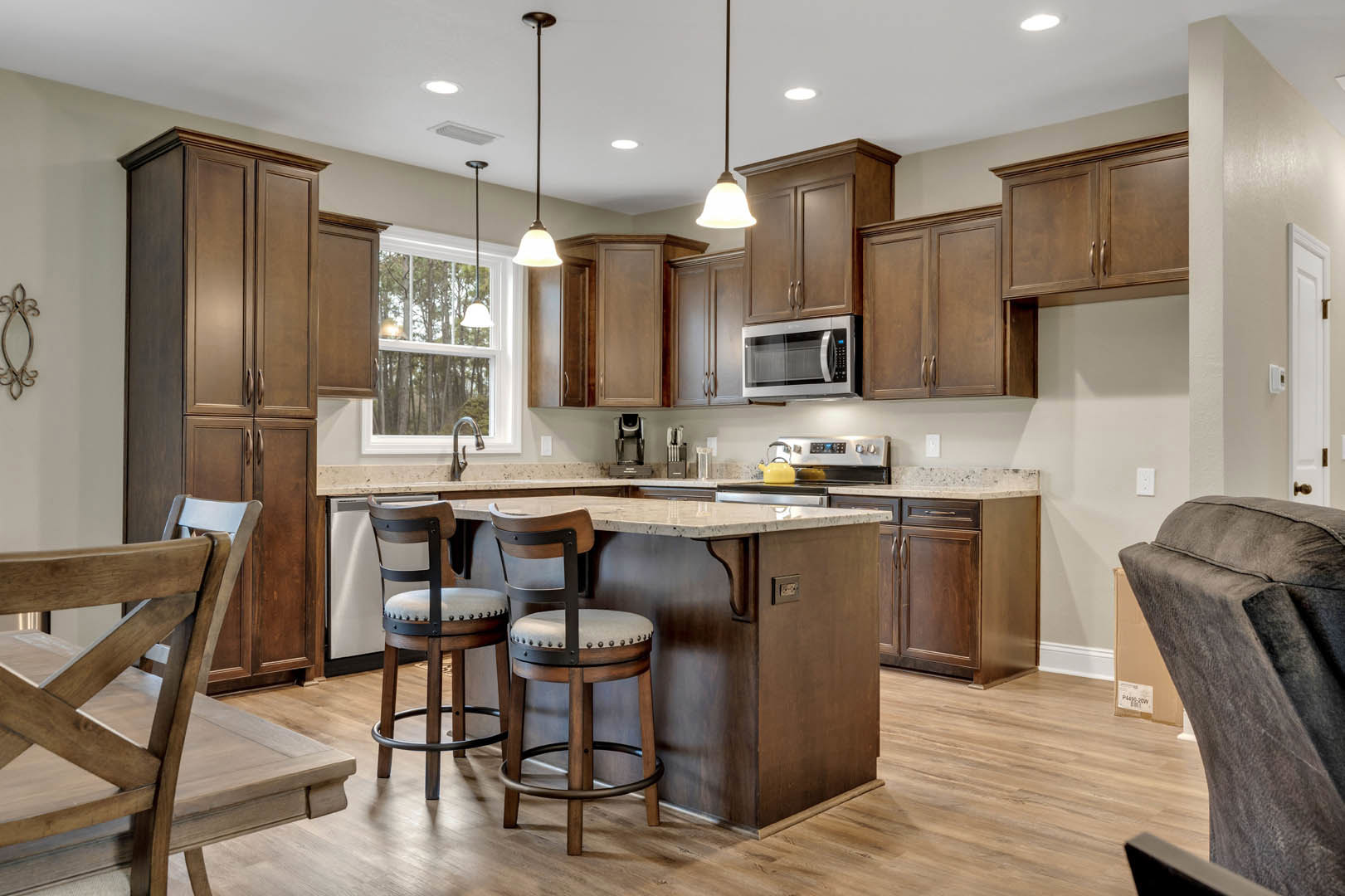 Modern kitchen with light wood cabinetry, stone countertops, built-in microwave, bar seating with white cushioned stools, and neutral walls.