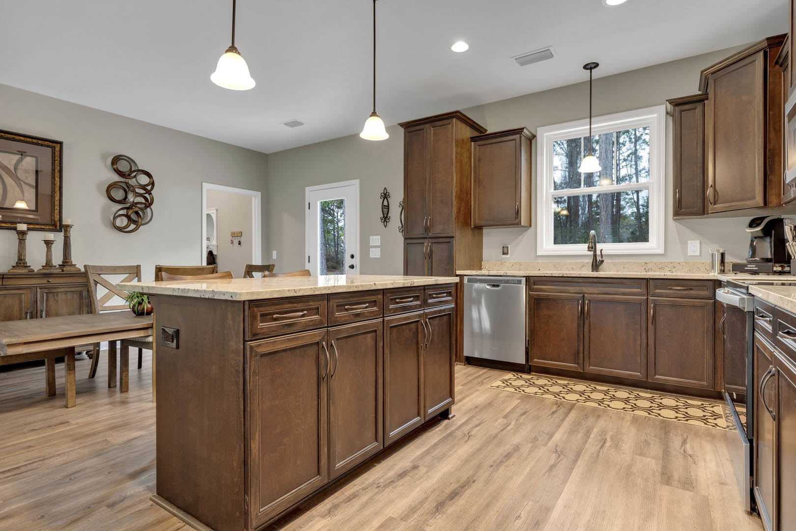 Kitchen with natural wood cabinets, matching wood floor, marble-topped island, stainless steel sink beneath a window, white refrigerator, and framed artwork on the wall