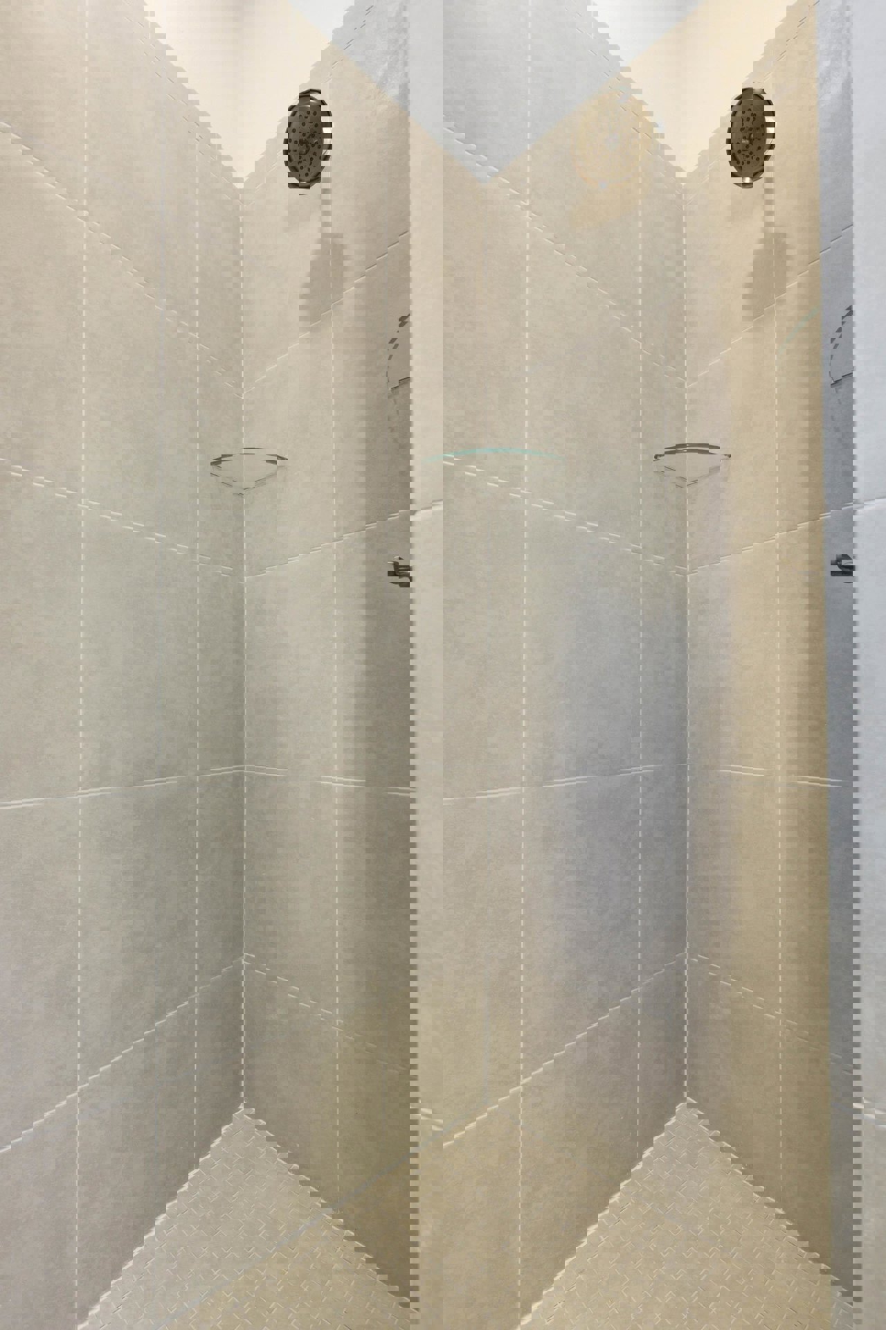 Shower with glass shelf, chrome shower head, white marble tile walls, green shampoo tube on built-in shelf, close-up of light gray tile floor