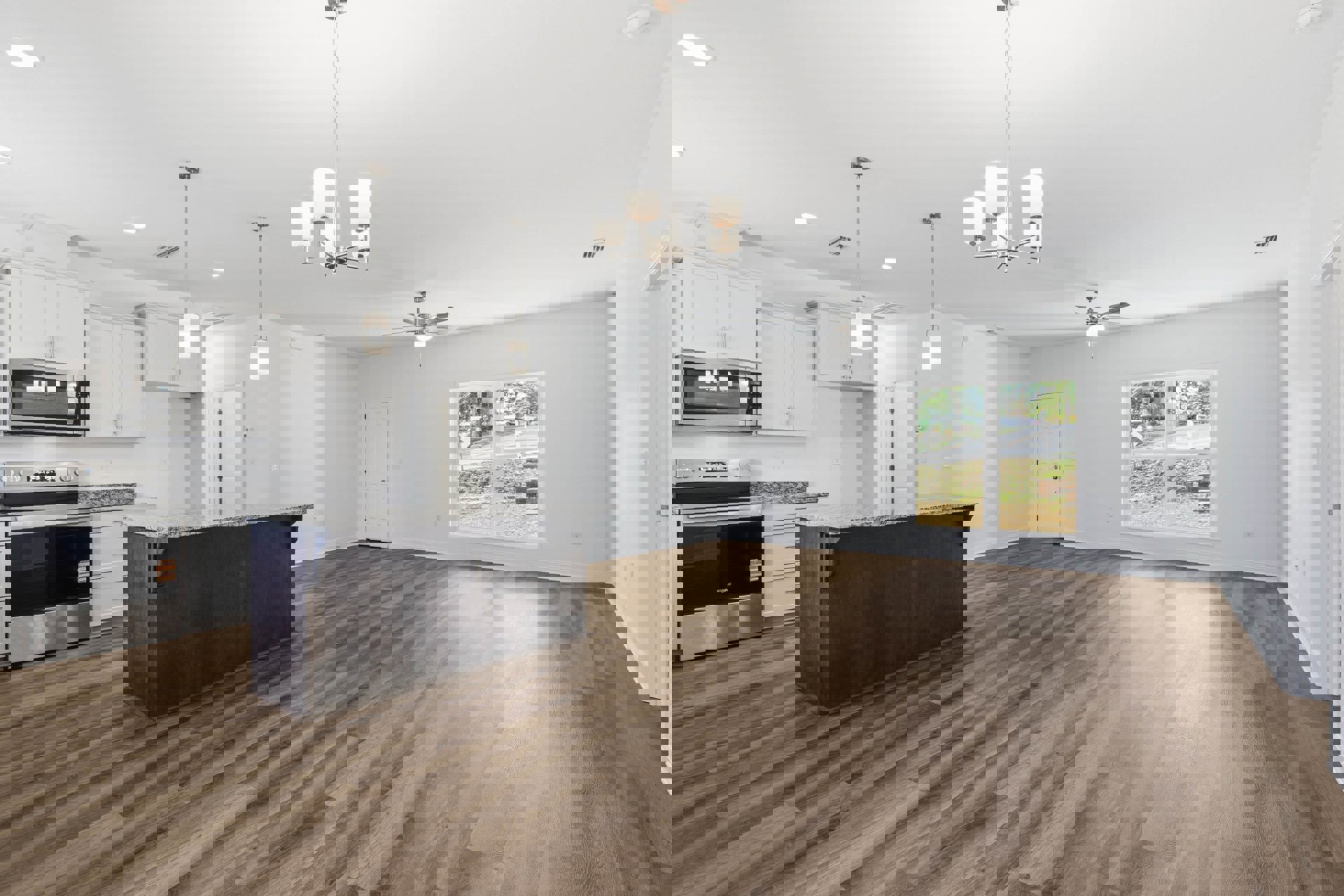 Kitchen with hardwood flooring, white walls, black countertop, stainless steel oven with black glass door, kitchen island, wall-mounted light fixtures, white door with silver knobs