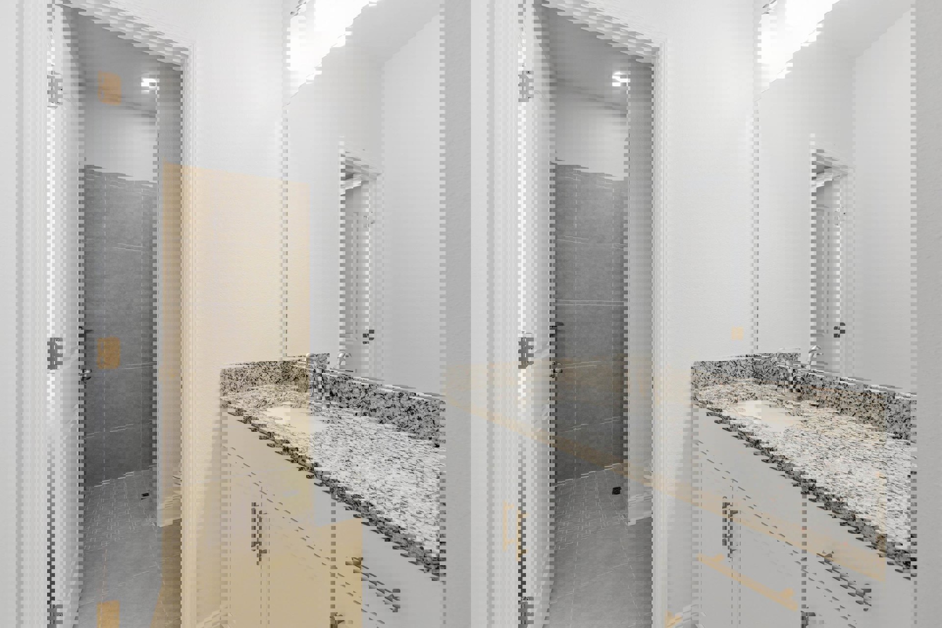 Bathroom with marble countertop, white sink, black speckled surface, wood cabinets, glass shower enclosure, white door with metal hinge and handle