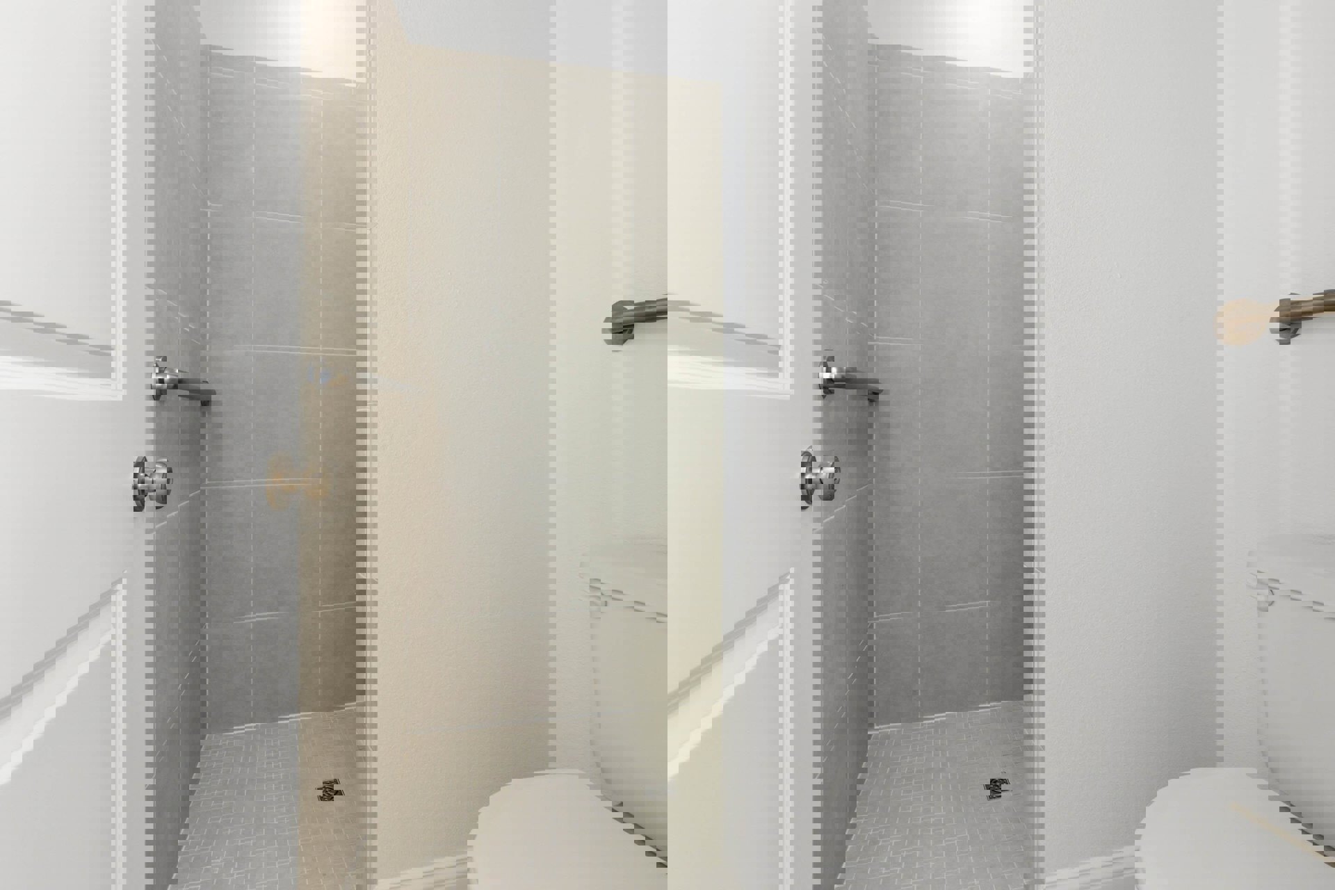 White tile bathroom with glass shower enclosure, modern toilet, chrome fixtures, and wood door with metal handle