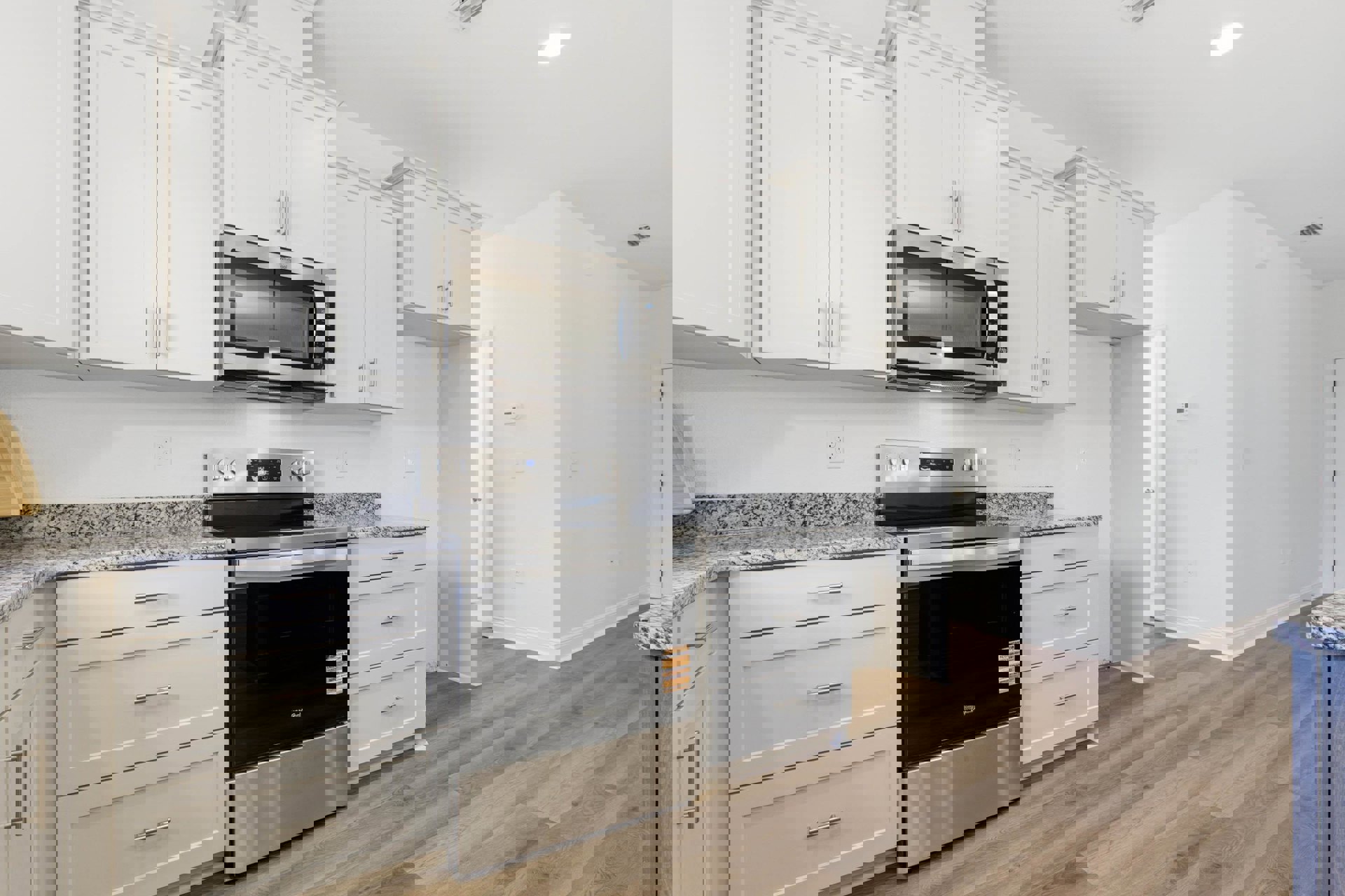 White kitchen with shaker cabinets, black appliances, marble countertops, stainless steel oven with black door, microwave above, wood flooring, and bright overhead lighting.