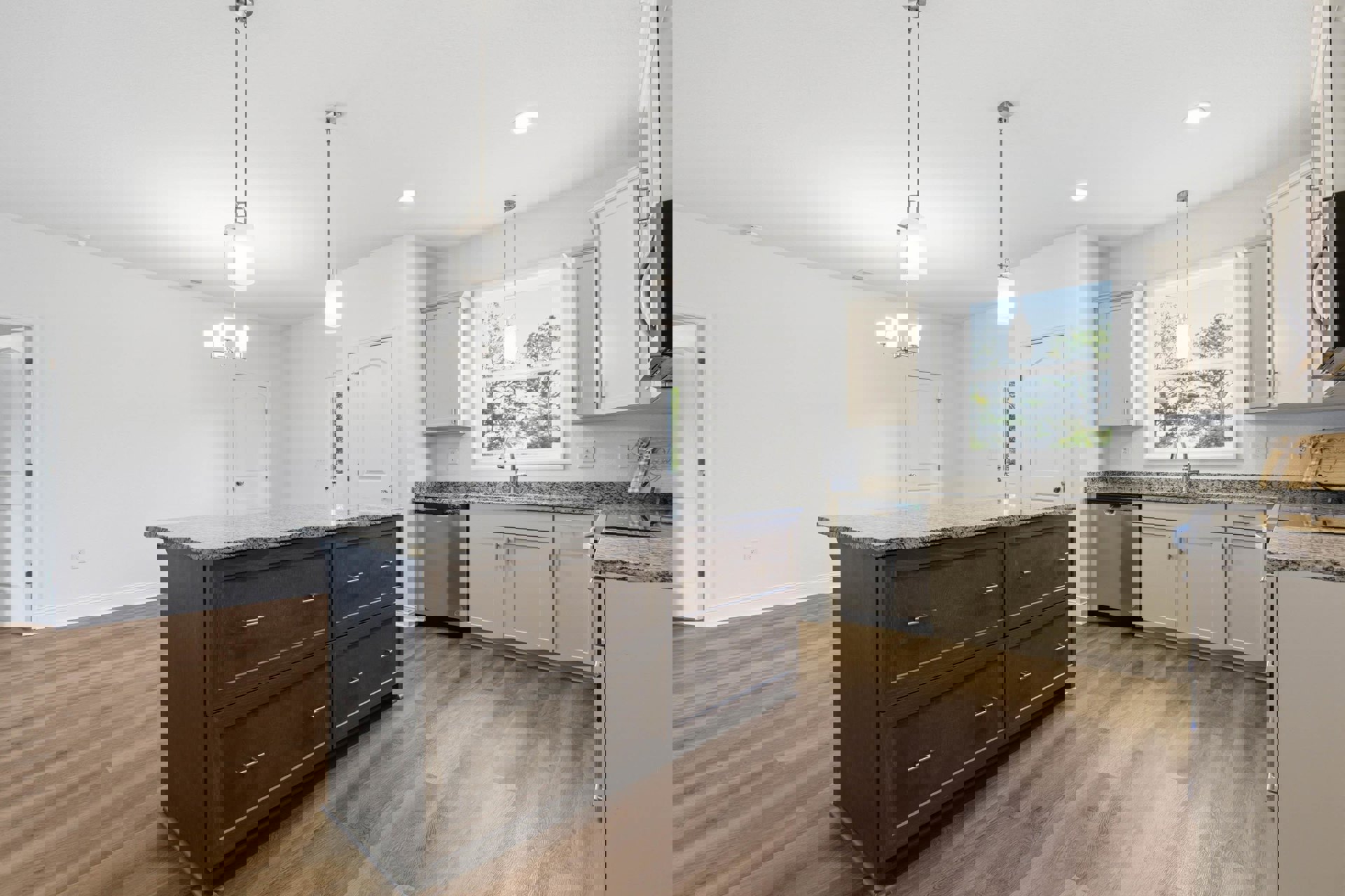 Spacious kitchen featuring a large central island with built-in sink, wood flooring, white cabinetry with drawers, stainless steel dishwasher, overhead ceiling light, and a white