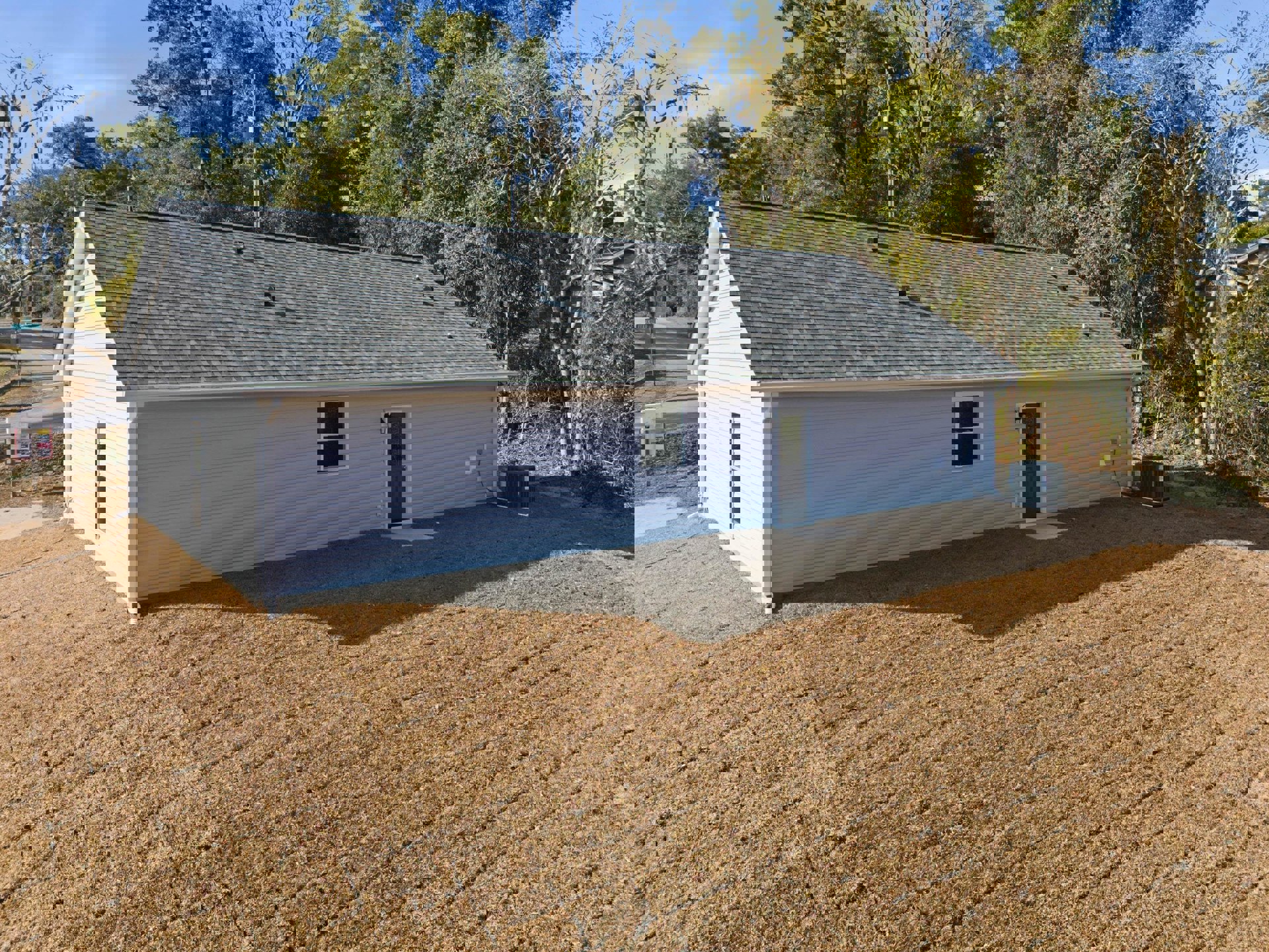 Light blue roof house with white-framed windows, large bare dirt patch in front yard, small lawn area, roadside black utility box, and close-up sign near property.