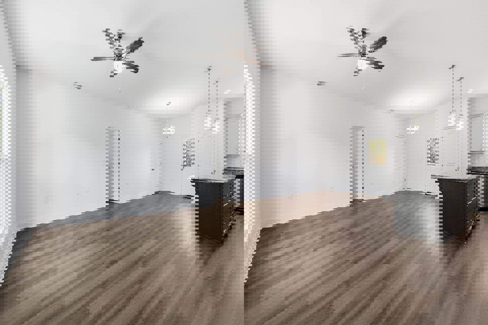 Open living area with wood flooring, ceiling fan with light, upright piano against a wall, black kitchen island with drawers, white doors featuring black and silver handles