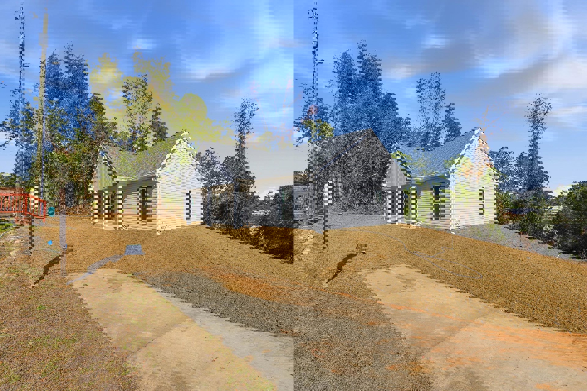 Two-story house with white roof, white-framed windows, wooden railing, driveway, green lawn, and mature trees under partly cloudy sky