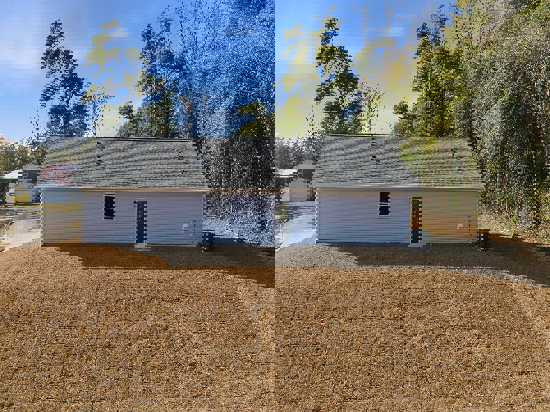 Two-story house with white siding, black front door, large windows, manicured lawn, mature trees in the background, and cloudy sky overhead