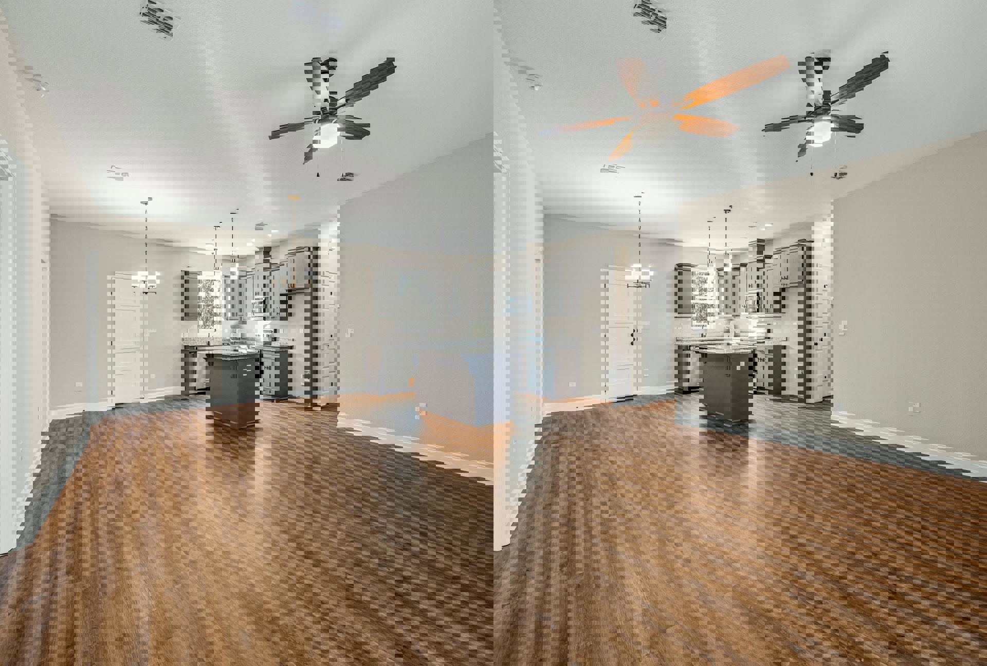 Spacious kitchen and dining area featuring wood flooring, marble-topped kitchen island, ceiling fan with light, white door with black hardware, and neutral walls.