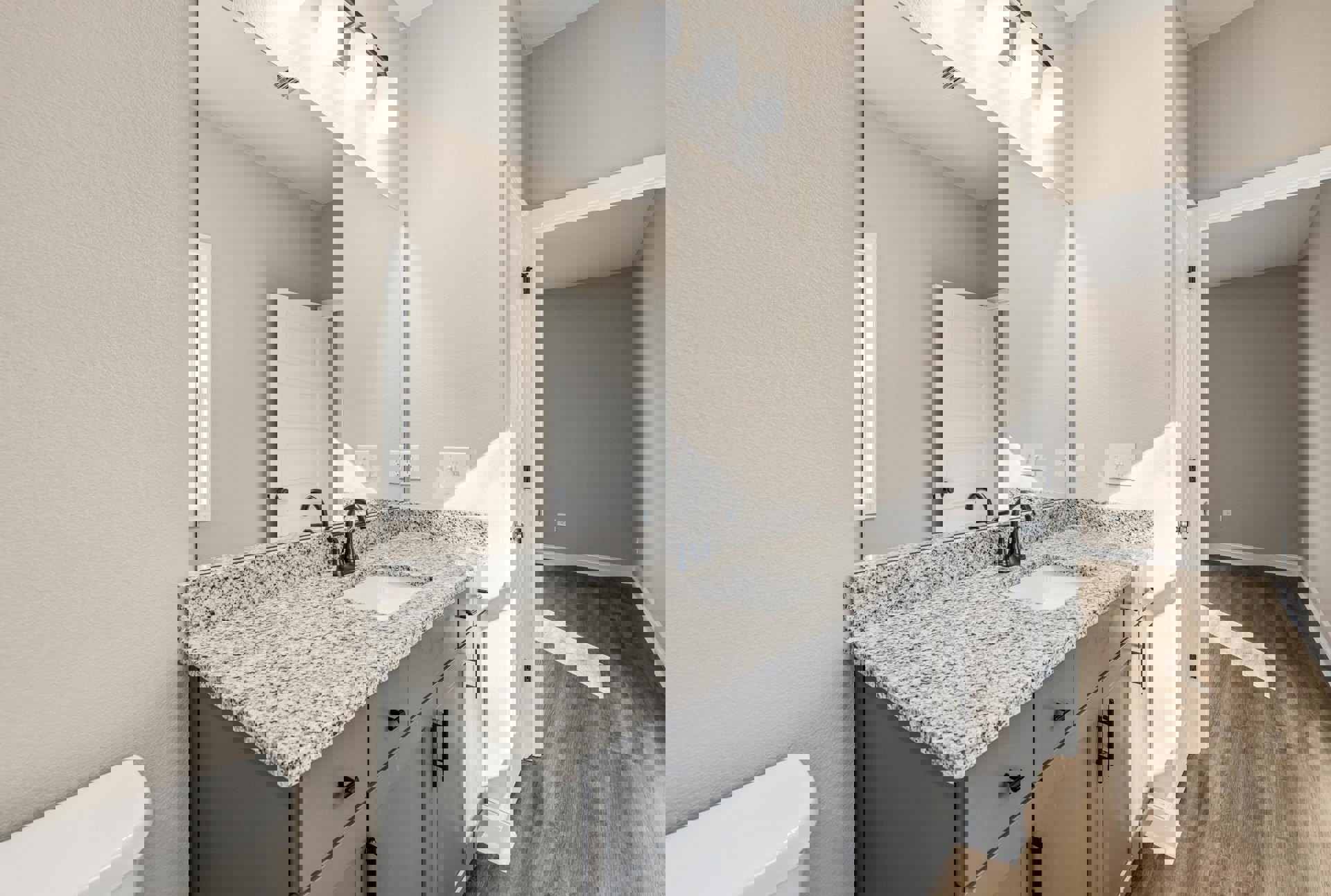 Marble countertop with white square sink, large wall mirror above, white bathtub and door, black and white speckled surface, tile flooring, cabinetry, and modern lighting fixture