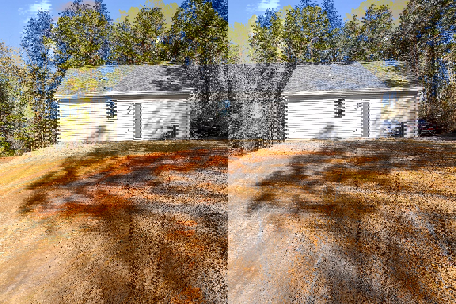 Single-story rural home with grey door and four-panel white door, front window illuminated, dirt driveway with tire tracks, black truck parked, surrounded by grass and trees under