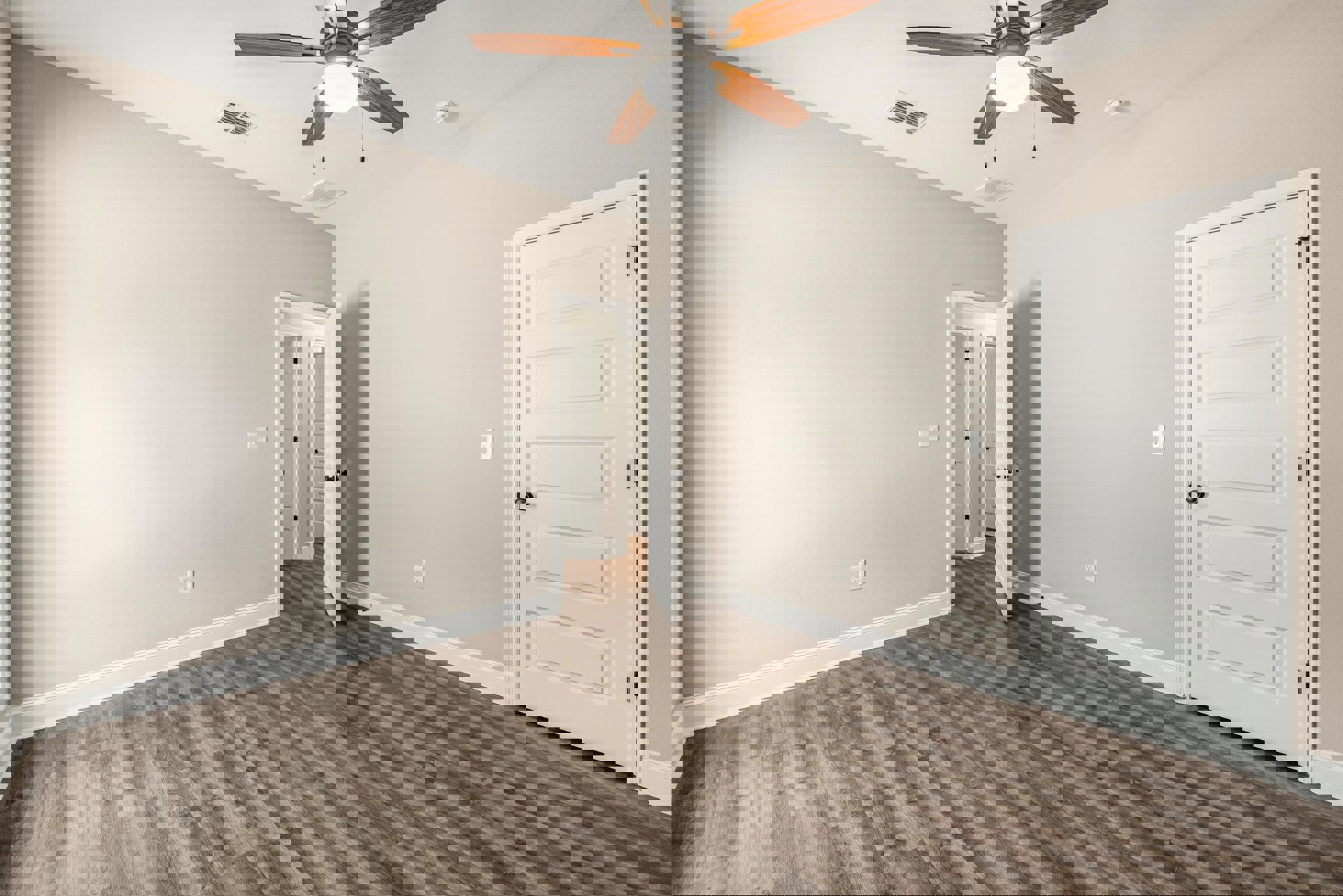 Wood flooring room with white doors featuring black knobs, ceiling fan with light fixture, wall vent on white plaster surface