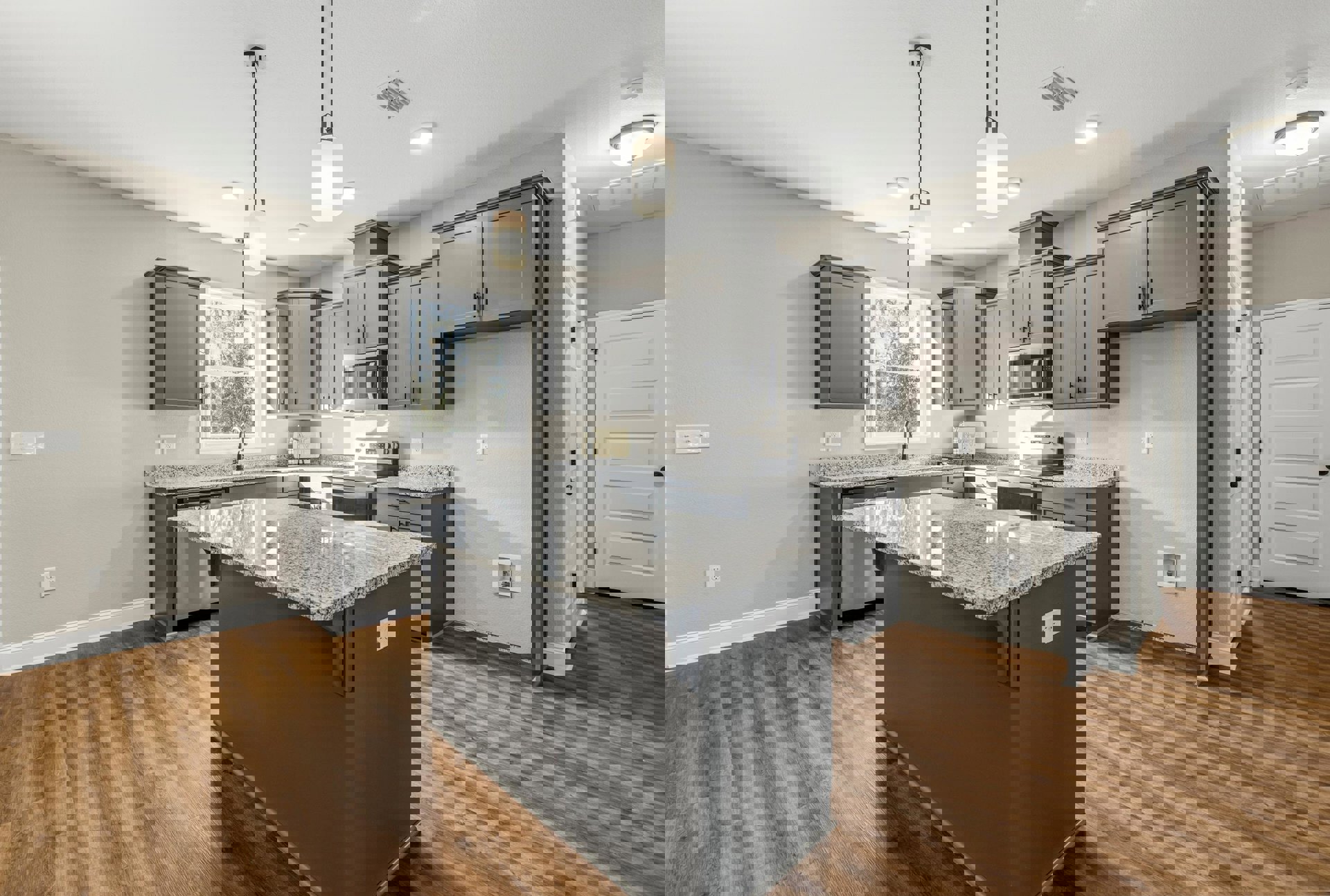 Marble kitchen island with waterfall edge, grey cabinetry, stainless microwave, white door with black handle, window above sink, pendant light fixture, hardwood flooring