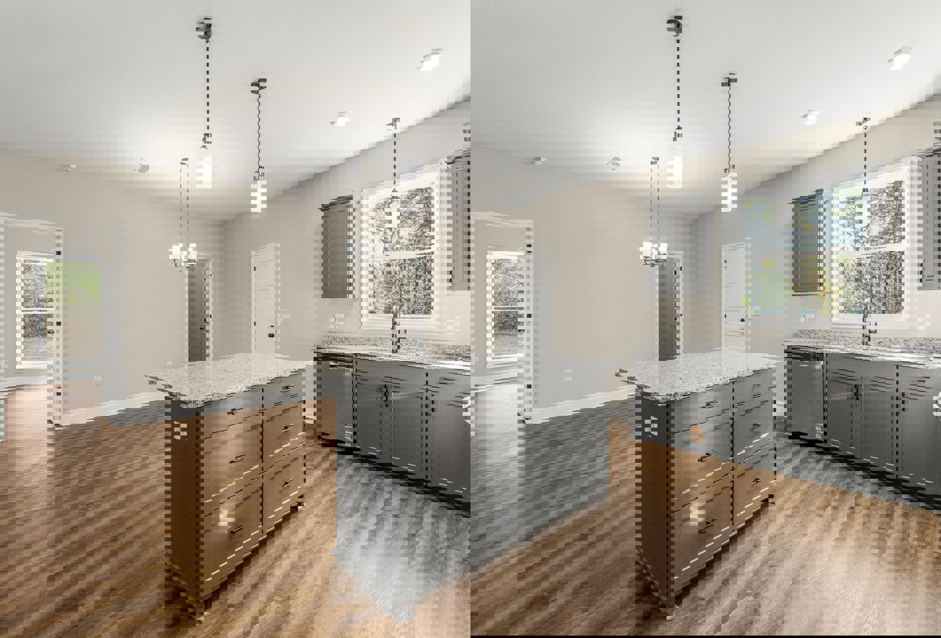 Spacious kitchen featuring a large island with drawers, white cabinetry, window above the sink, white light fixture with black top, grey door with black handle, and white door with