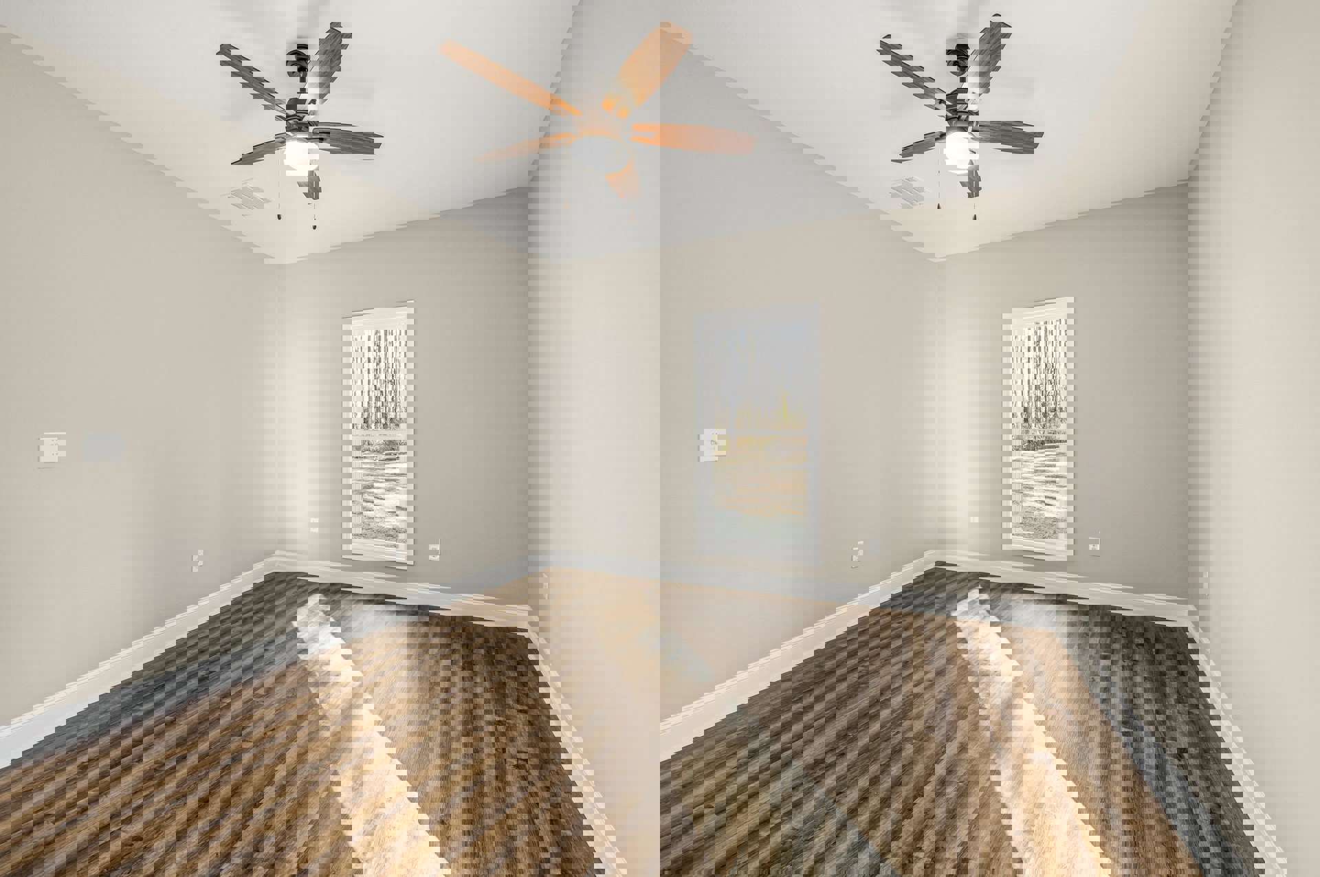 Ceiling fan with integrated light above wood flooring, white baseboards, and a window framing leafy trees outside