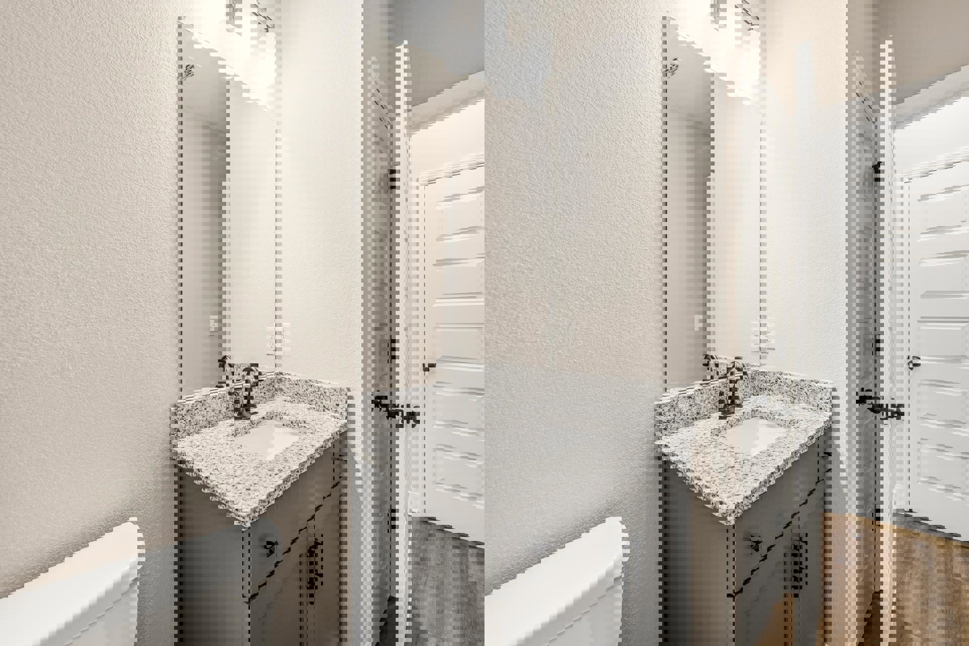 White bathroom featuring a speckled black and white countertop, undermount sink, white cabinetry, modern black faucet, white toilet, and white door with black handle against smooth