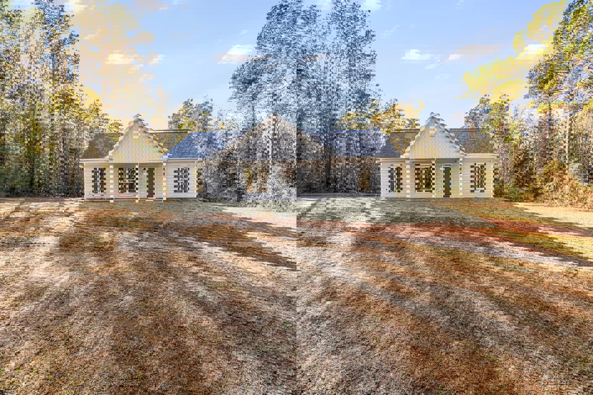 White house with black front door, large window with white frame, expansive green lawn, mature tree, blue sky with scattered clouds