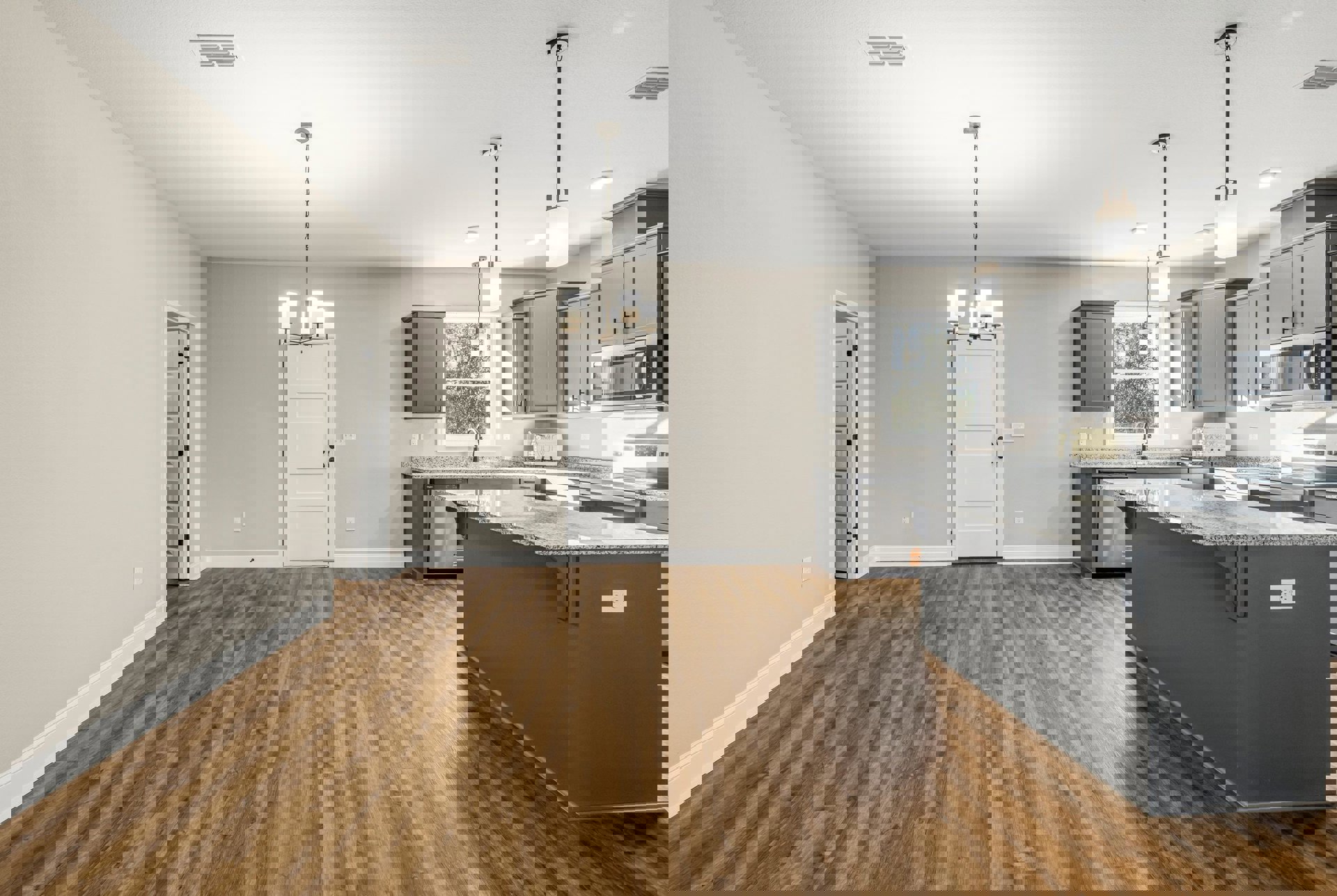 Kitchen with wood flooring, white cabinetry, marble-topped island, white door with black knobs, stainless steel microwave with glass door, window above sink, pendant light fixture