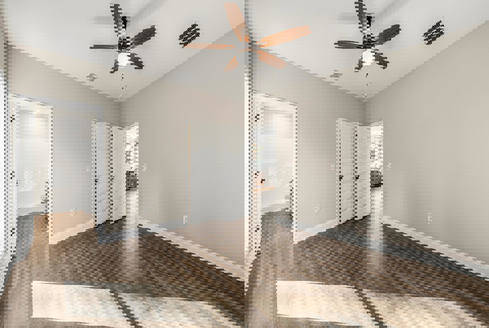 Ceiling fan with light fixture, wood laminate flooring, white doors with black knobs, white bathroom visible with toilet and tub, ceiling vent, neutral walls