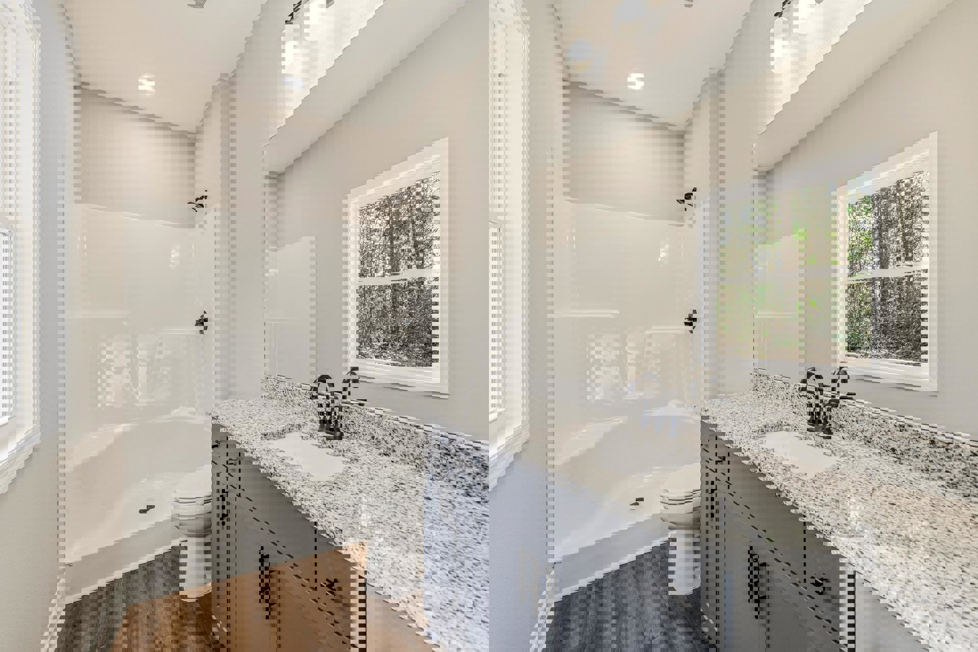 Bathroom with white tile walls, a white toilet with seat down, rectangular sink on a stone countertop, black metal towel bar, window overlooking trees, and glass shower enclosure.