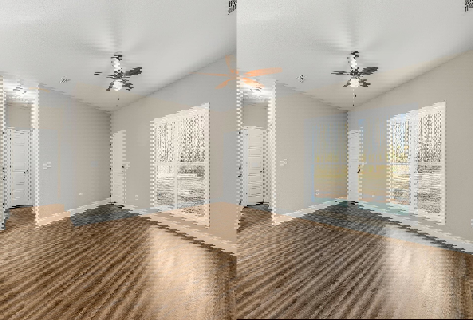 Wood flooring, ceiling fan with light, white door featuring black handle and knobs, window overlooking trees, neutral walls and ceiling.