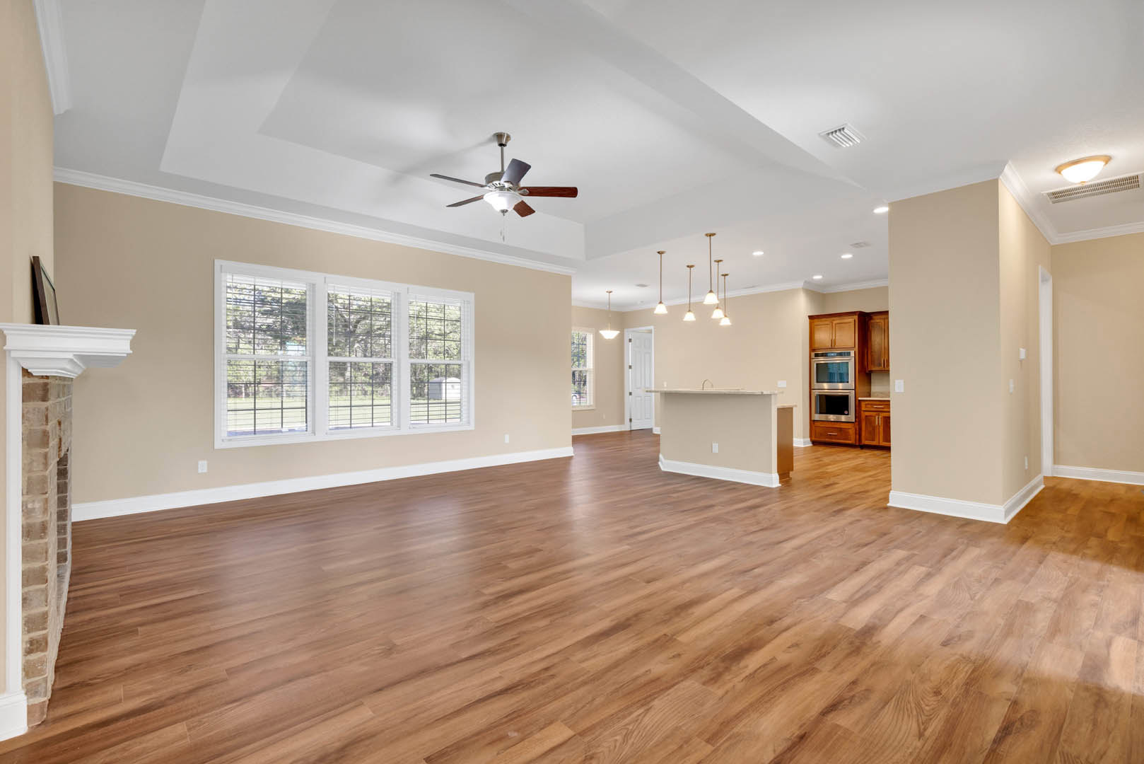 Spacious living room with rich hardwood flooring, neutral walls, ceiling fan with light fixture, and large windows allowing natural light
