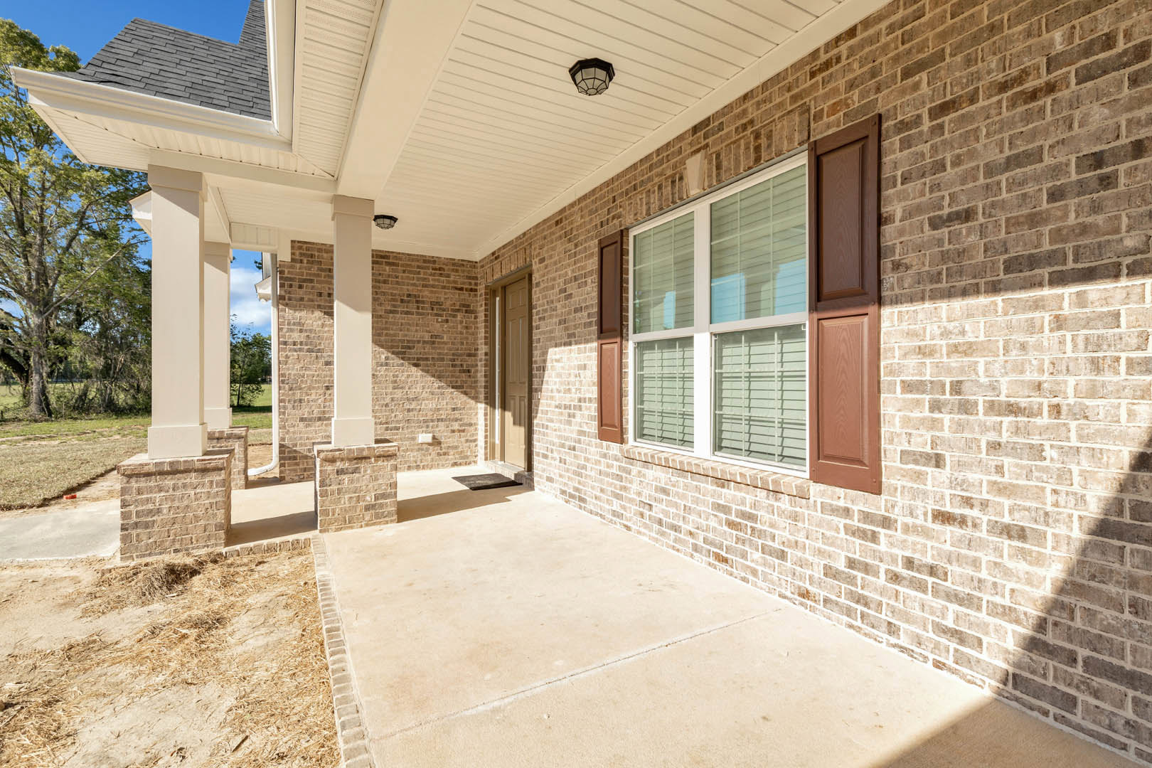 Red brick house with covered porch, white-framed windows, wooden front door, and leafy tree in front yard