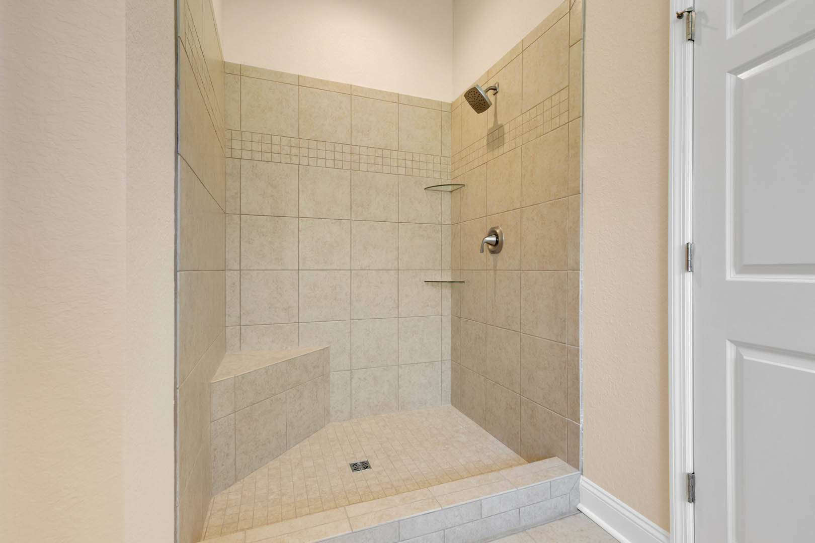 Walk-in shower with marble tile walls, chrome shower head, and matching handle, white plaster wall with black trim, and tile flooring with a circular drain