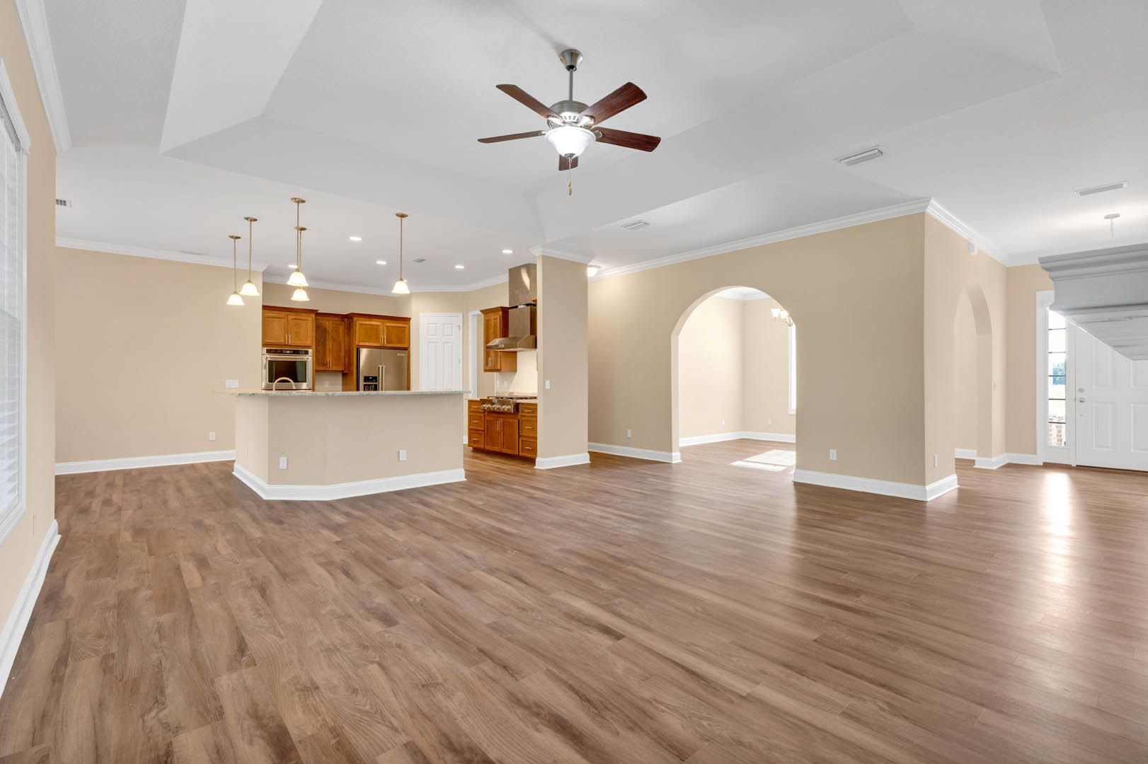 Open-concept room with hardwood flooring, ceiling fan with light fixture, white kitchen counter, stainless steel microwave, and refrigerator against a white wall