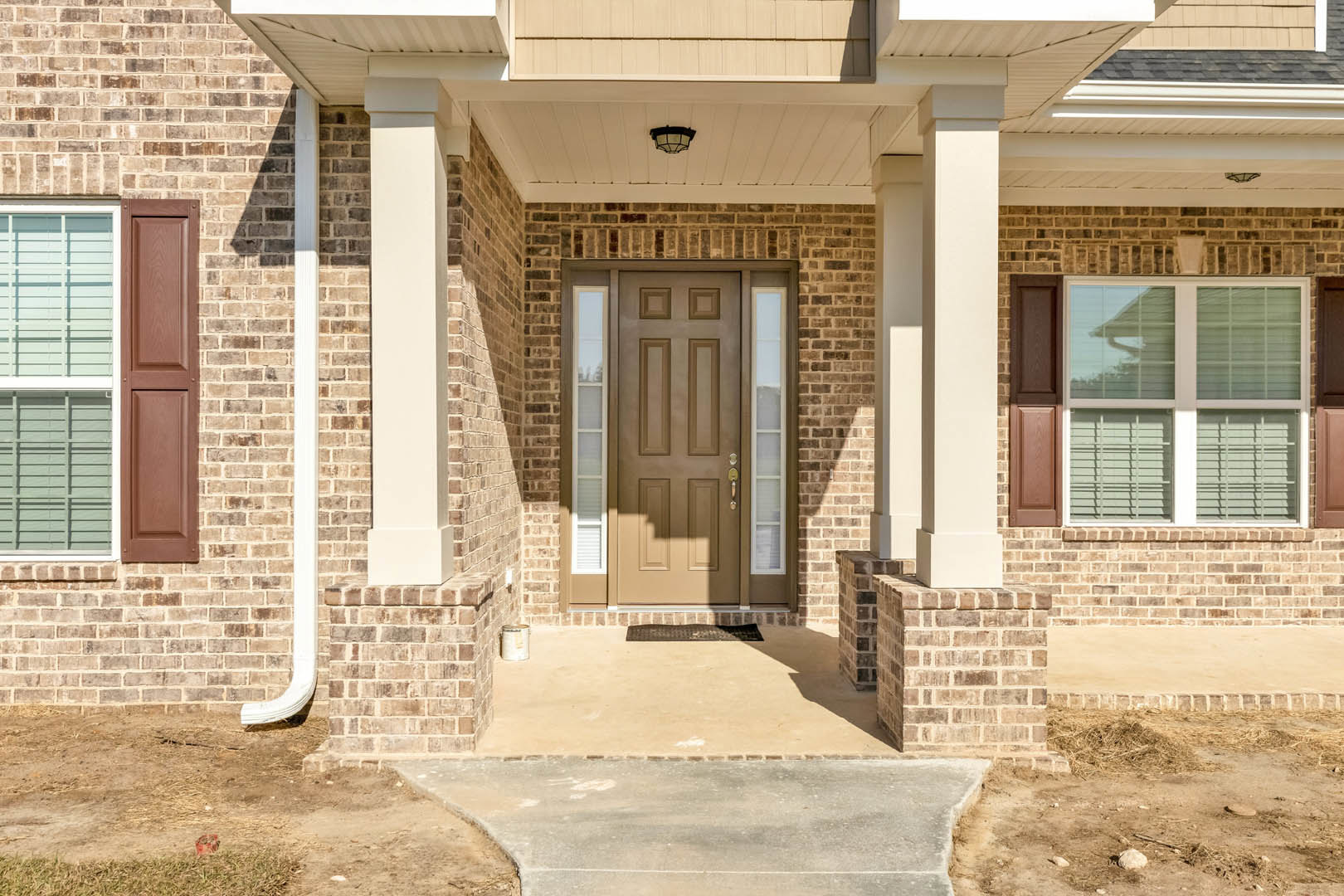 Brown front door with glass panes set in red brick exterior, adjacent window, concrete porch steps, and composite roof shingles