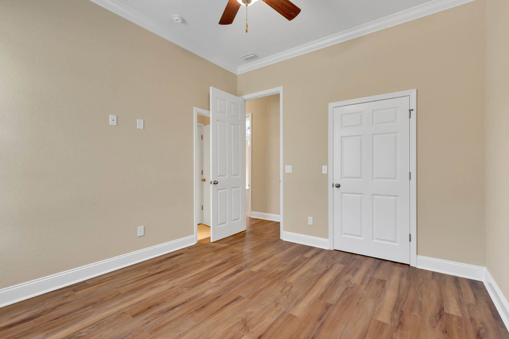Room with wood flooring, white trim, ceiling fan, and multiple white doors with silver and black handles