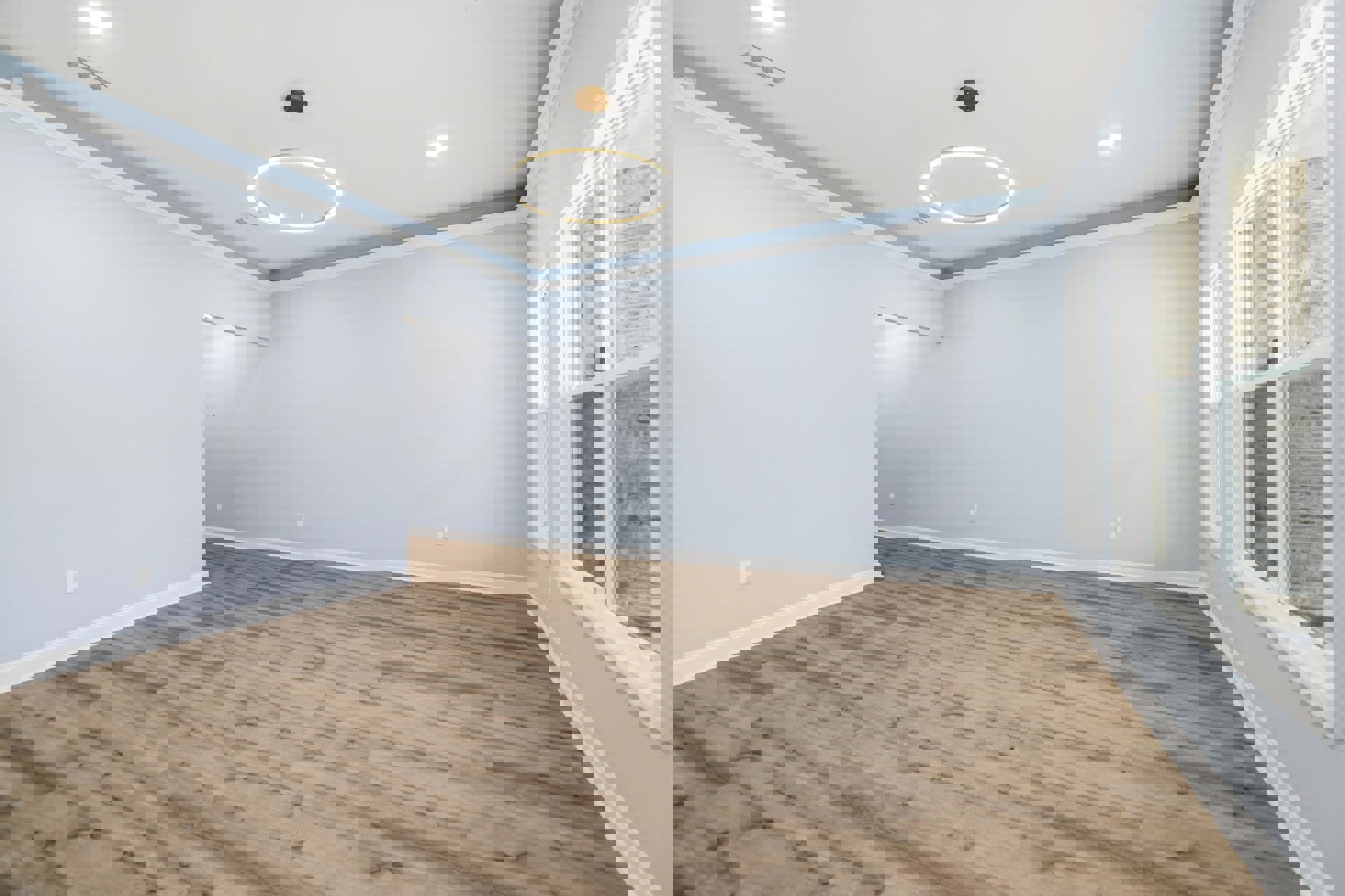 Wood flooring with white baseboards, circular ceiling light fixture, white brick accent wall, window framed in white overlooking exterior brick wall