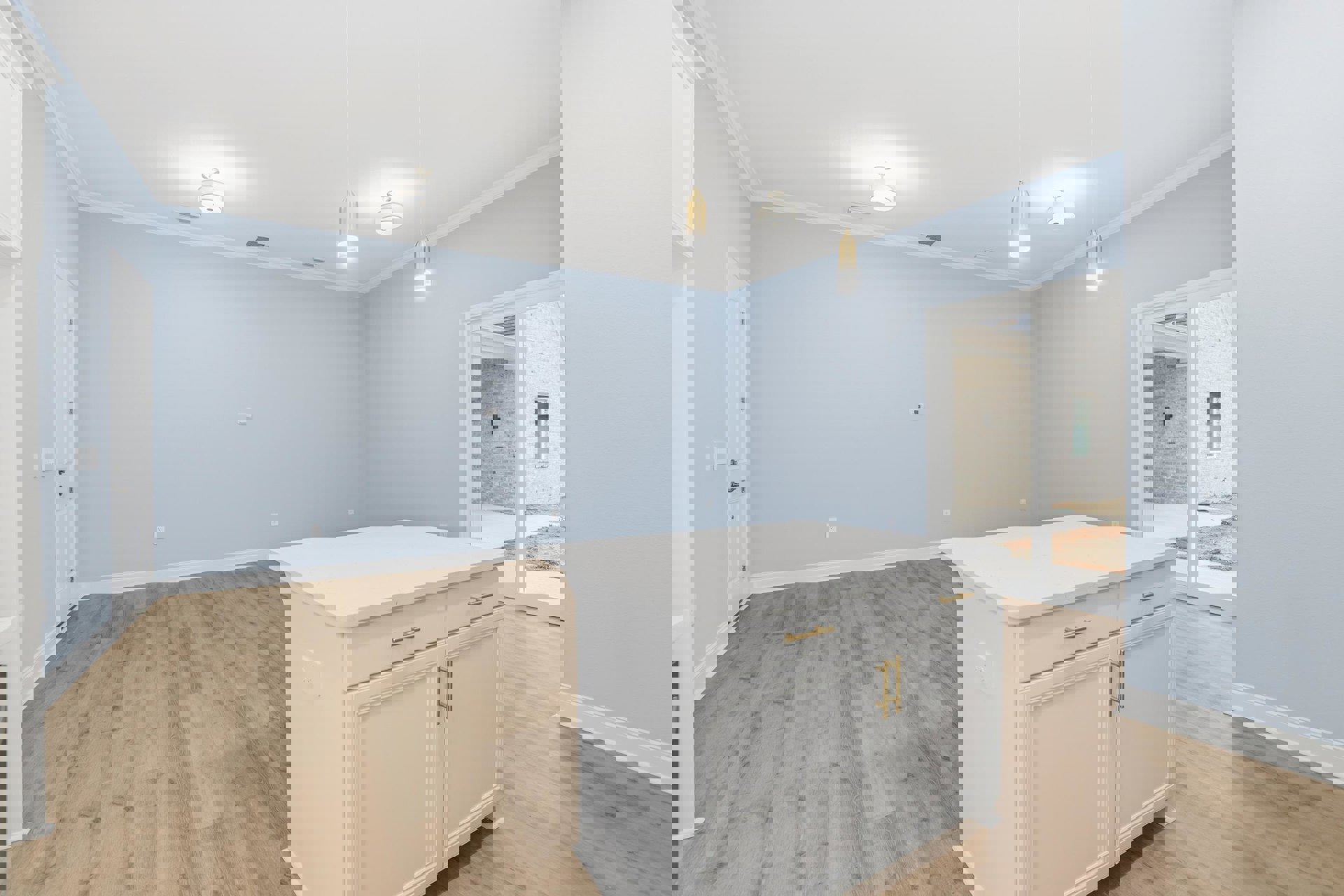 White kitchen island with gold handles, wood plank flooring, white cabinetry, white pendant light fixture, marble countertop, stainless steel sink, neutral walls.