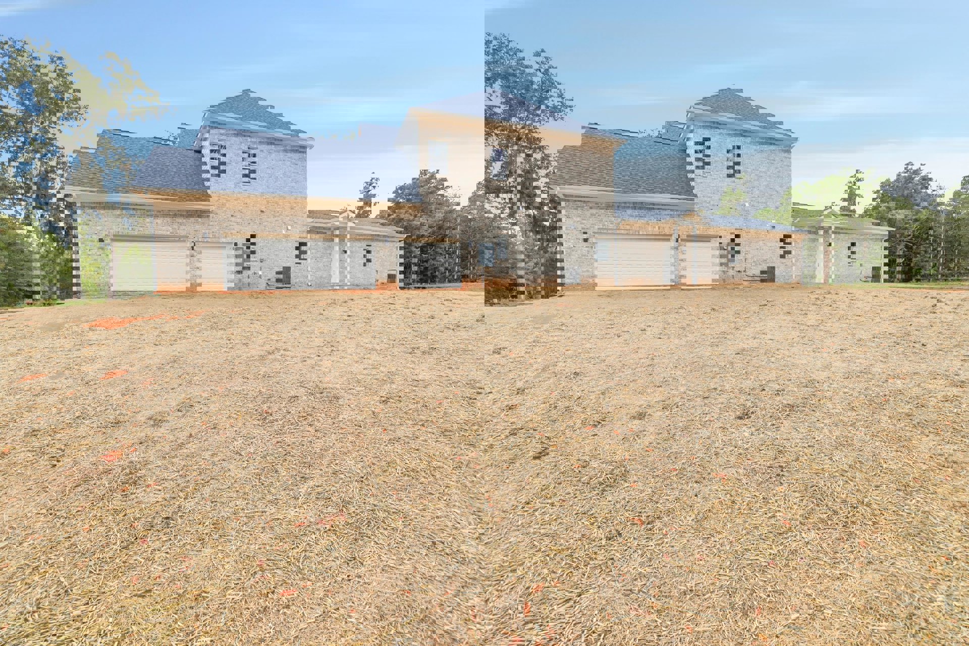 Brick house with white garage doors, large green lawn, mature tree, blue sky, and a man standing near the garage