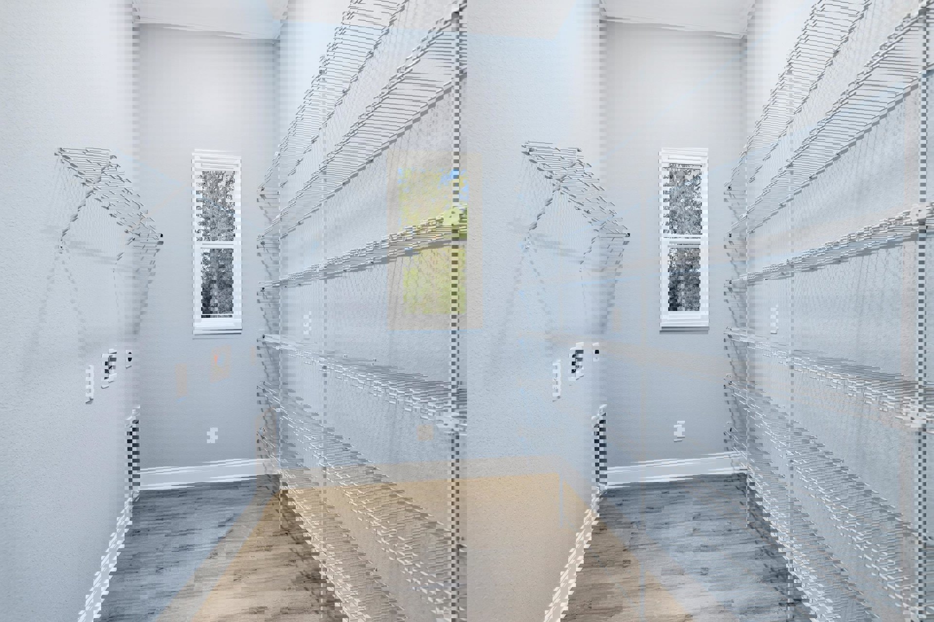 White built-in shelves along a plaster wall, wood floor, large window with trees visible outside, natural daylight filling the room.