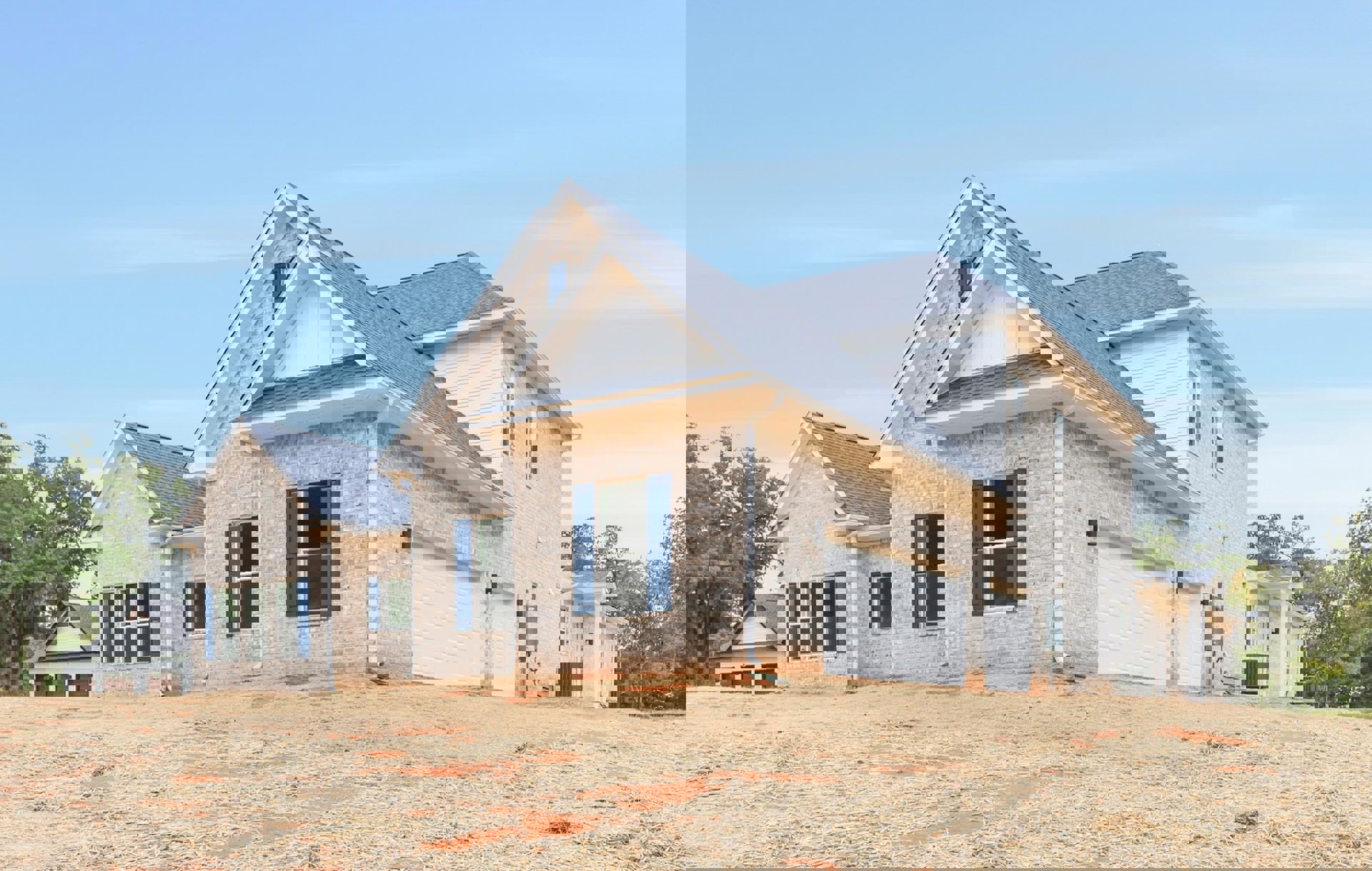 White siding house with blue shuttered windows, attached garage with paneled door, dirt landscaping in foreground, gabled roof, mature tree in background.
