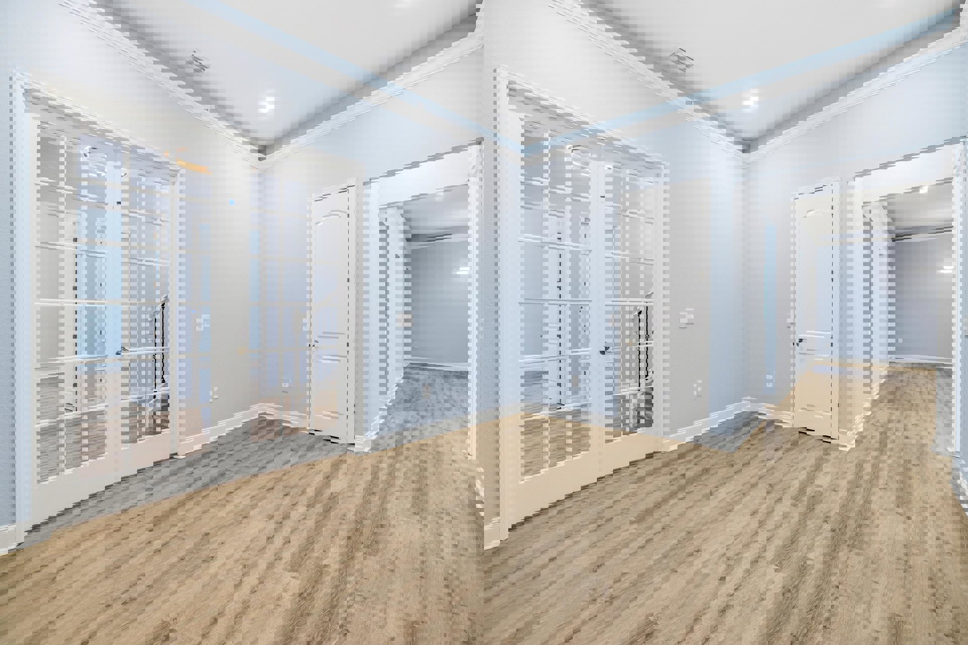 White doors with silver handles, wood laminate flooring, white plaster walls reflecting light, glass-paneled door, white ceiling with recessed light fixture.