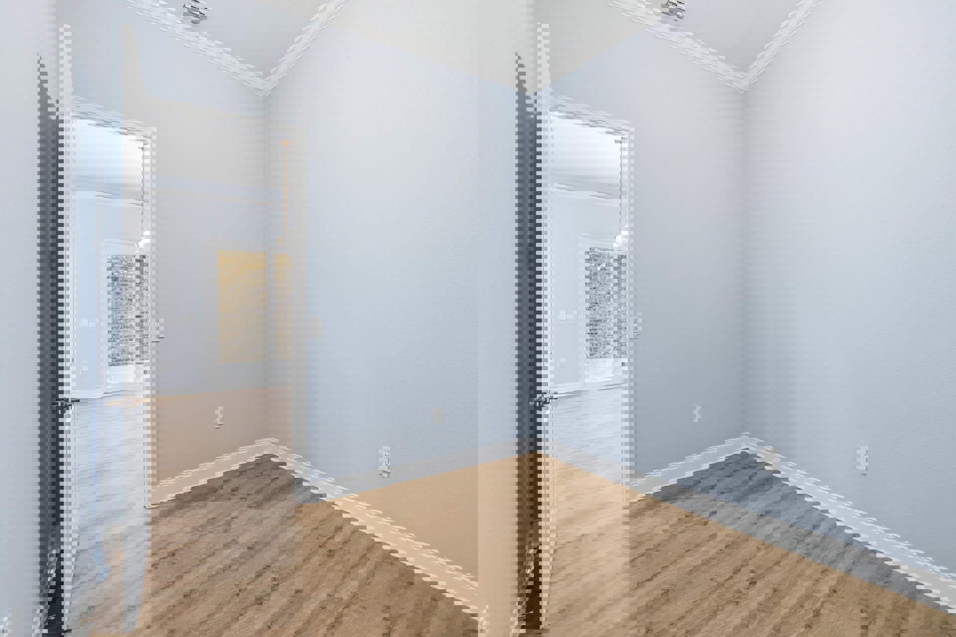 White paneled door open to a room with wood flooring, white baseboards, white walls, and ceiling with crown molding; wall-mounted light fixture near the doorway.