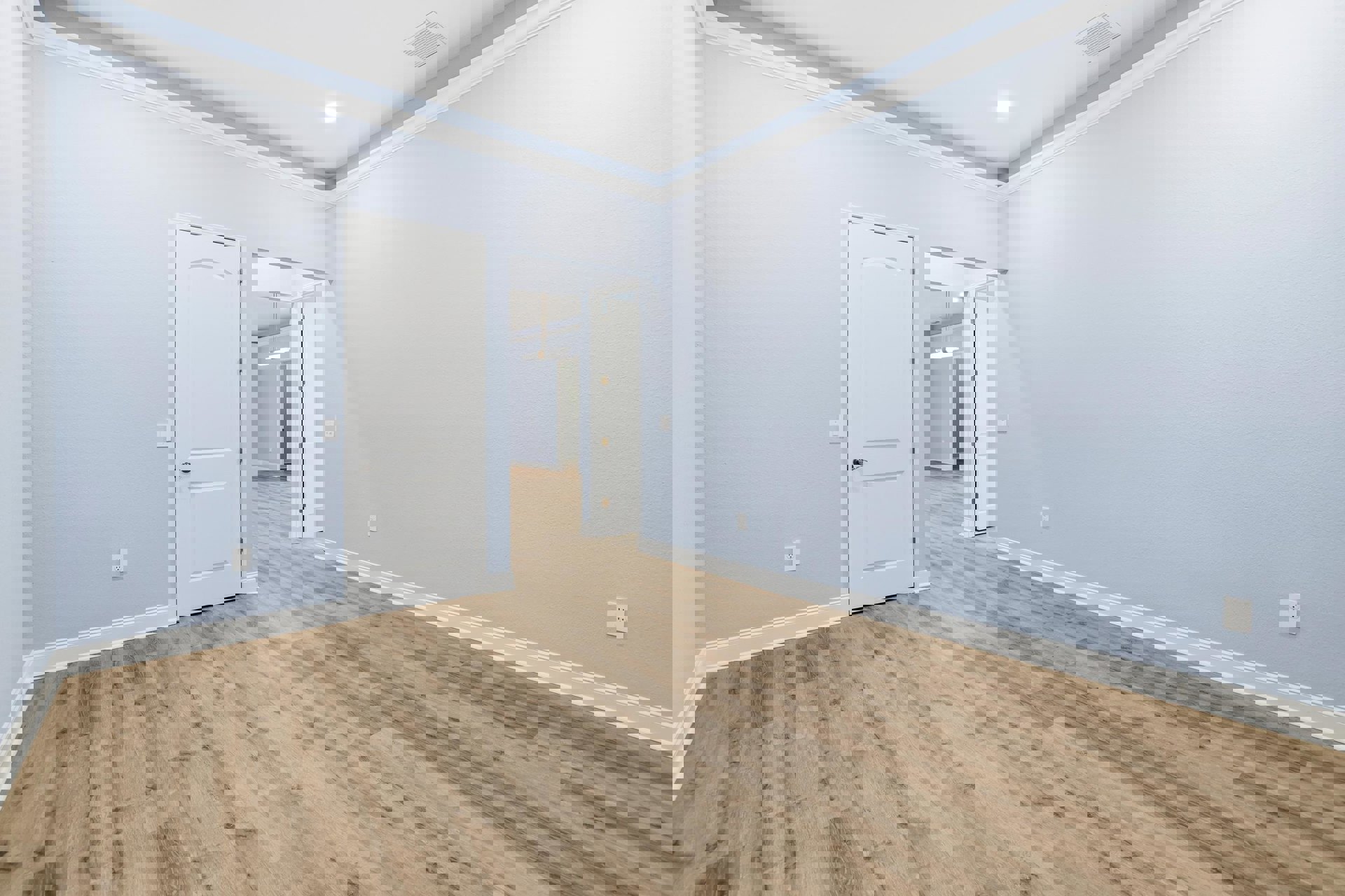 Light blue walls and wood laminate flooring, white door with silver handle, ceiling vent and recessed light, lamp mounted above door.