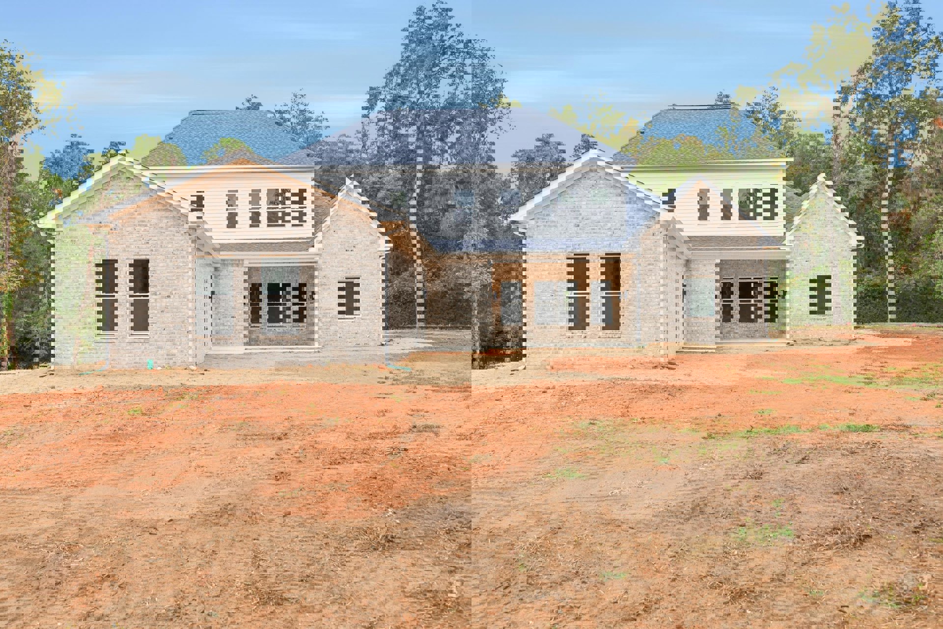 Single-story brick house with white-framed windows, white roof, and unfinished dirt yard under clear sky