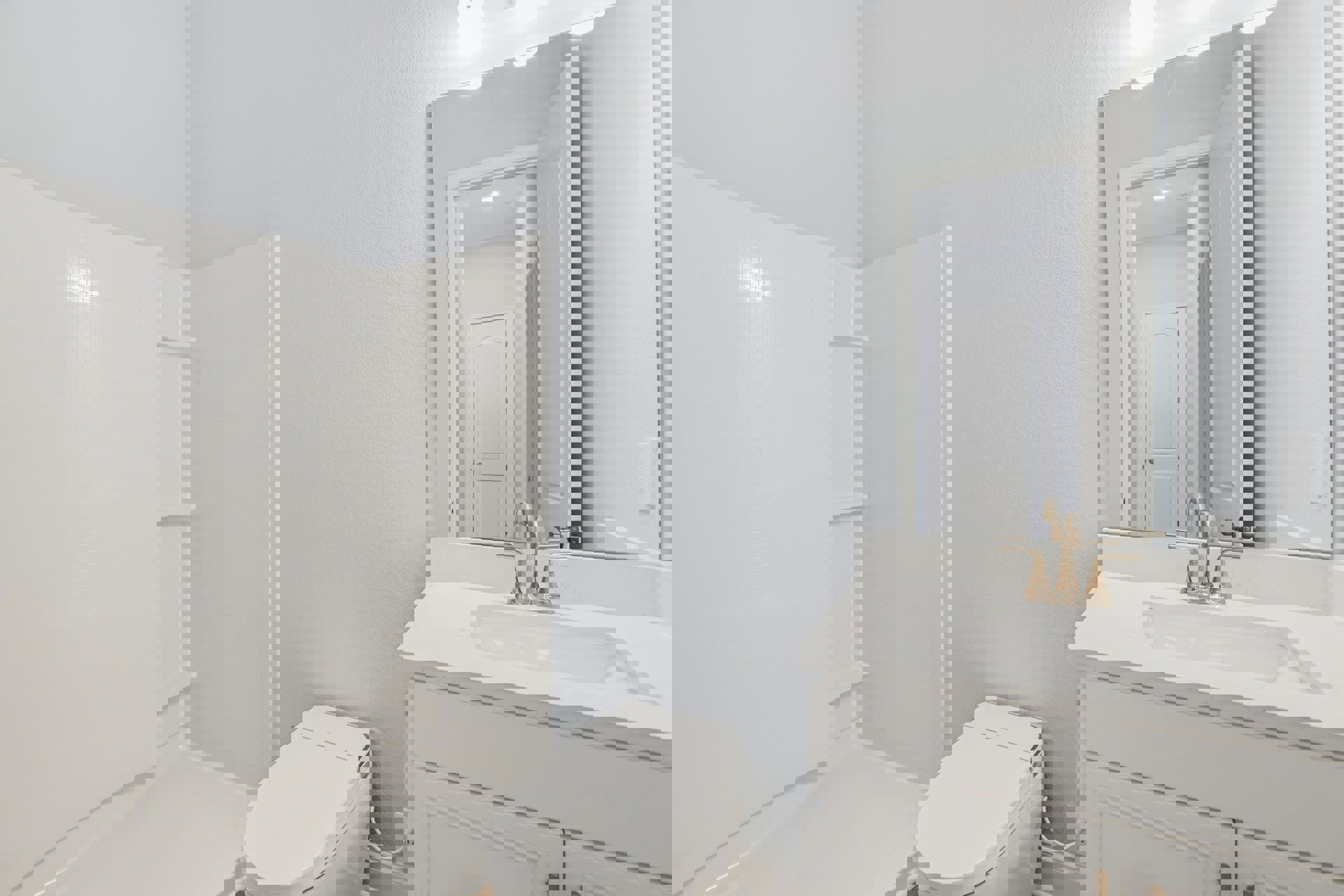 Bathroom with white toilet, rectangular sink and chrome faucet, wall-mounted mirror above sink, white door with lock, white shelves on wall, light tile flooring