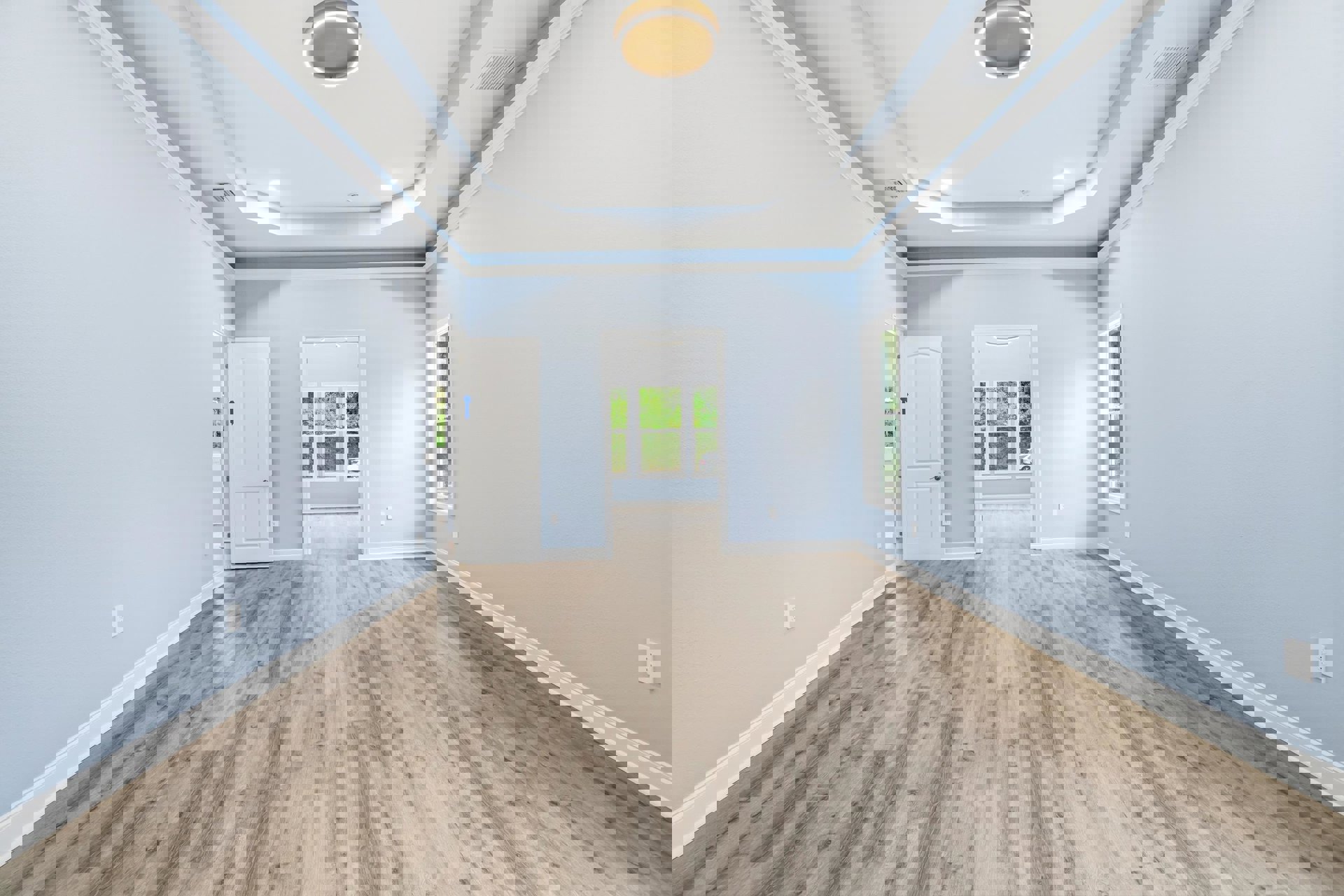 Wood floor with white paneled doors, circular ceiling light fixture, white wall vent, and molding along plaster walls