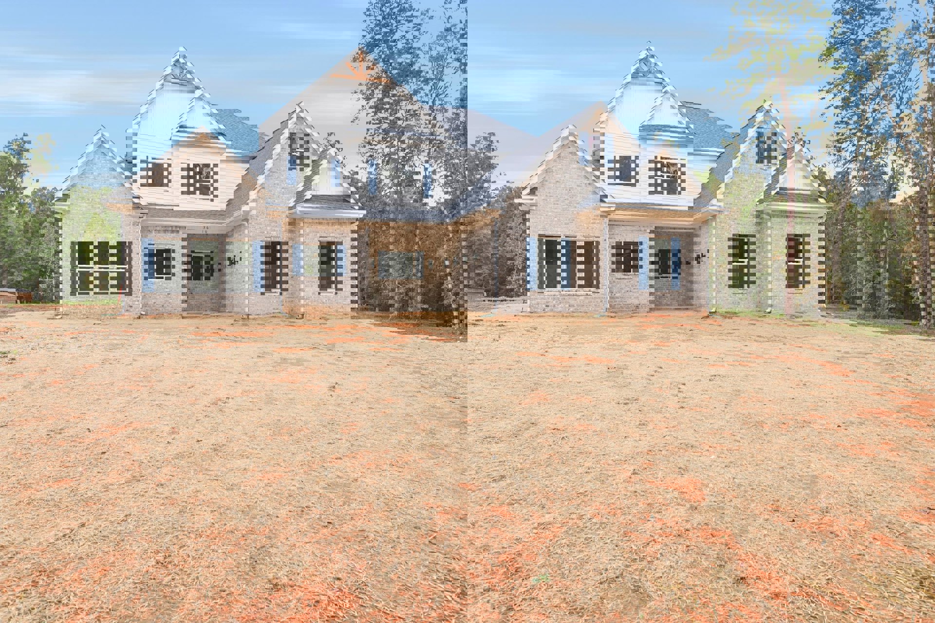 Brick house with white-framed windows and blue shutters, surrounded by a grassy yard and mature trees under a clear blue sky
